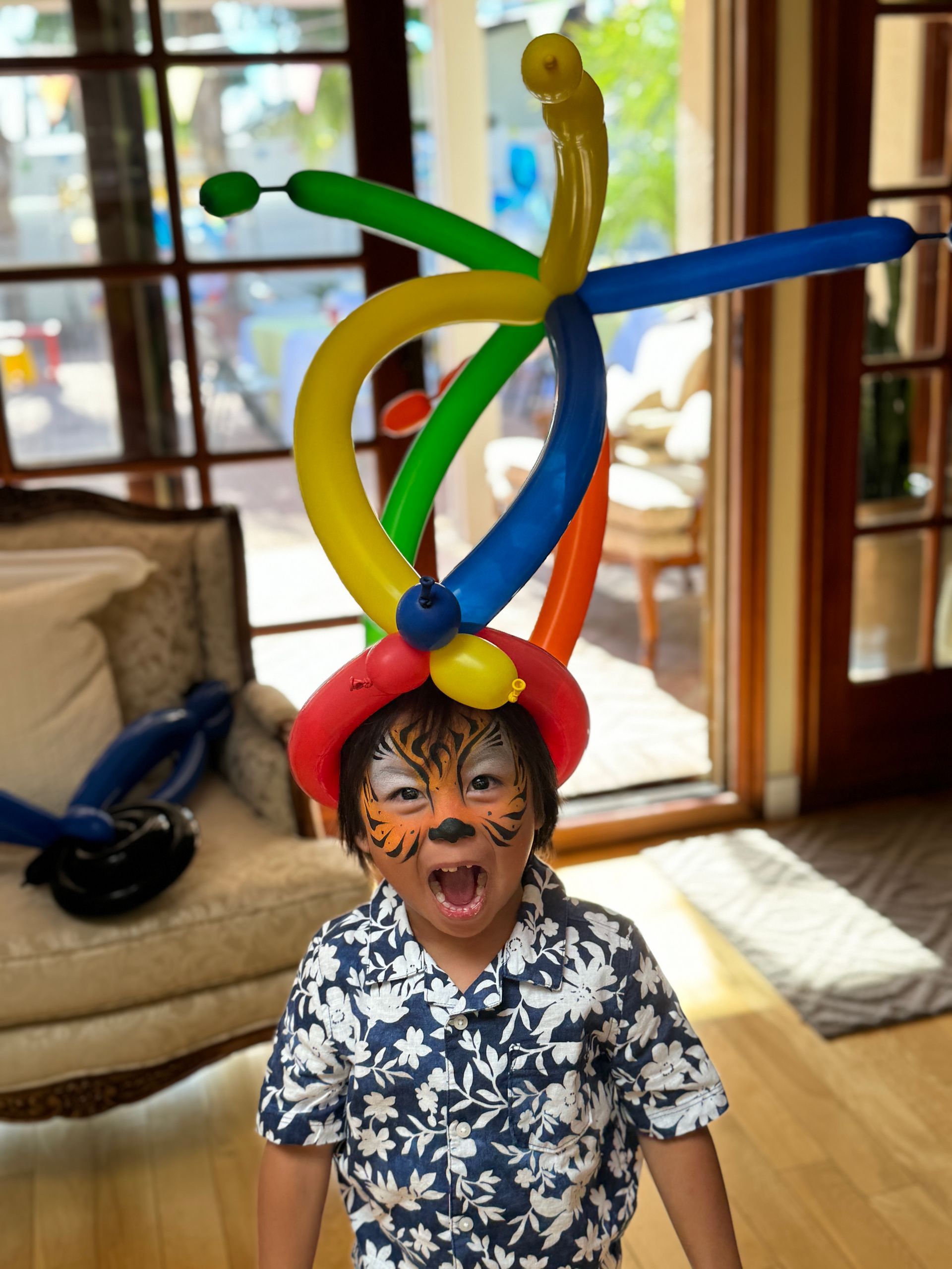 A young boy with face paint and a hat made of balloons