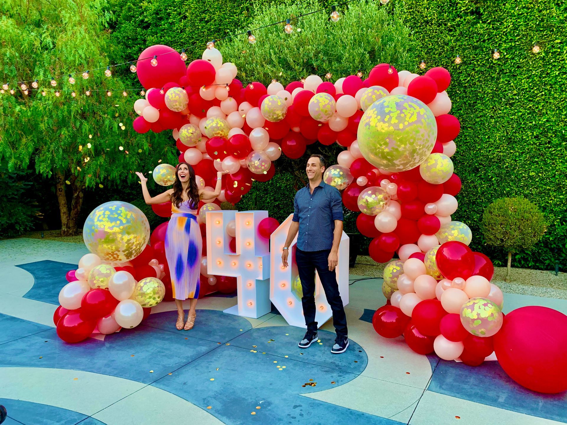 A man and a woman are standing in front of a balloon arch.