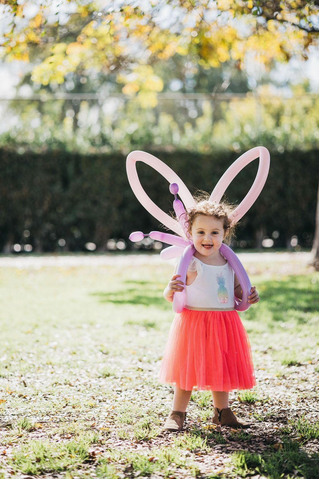 A little girl wearing balloon wings is standing in the grass.
