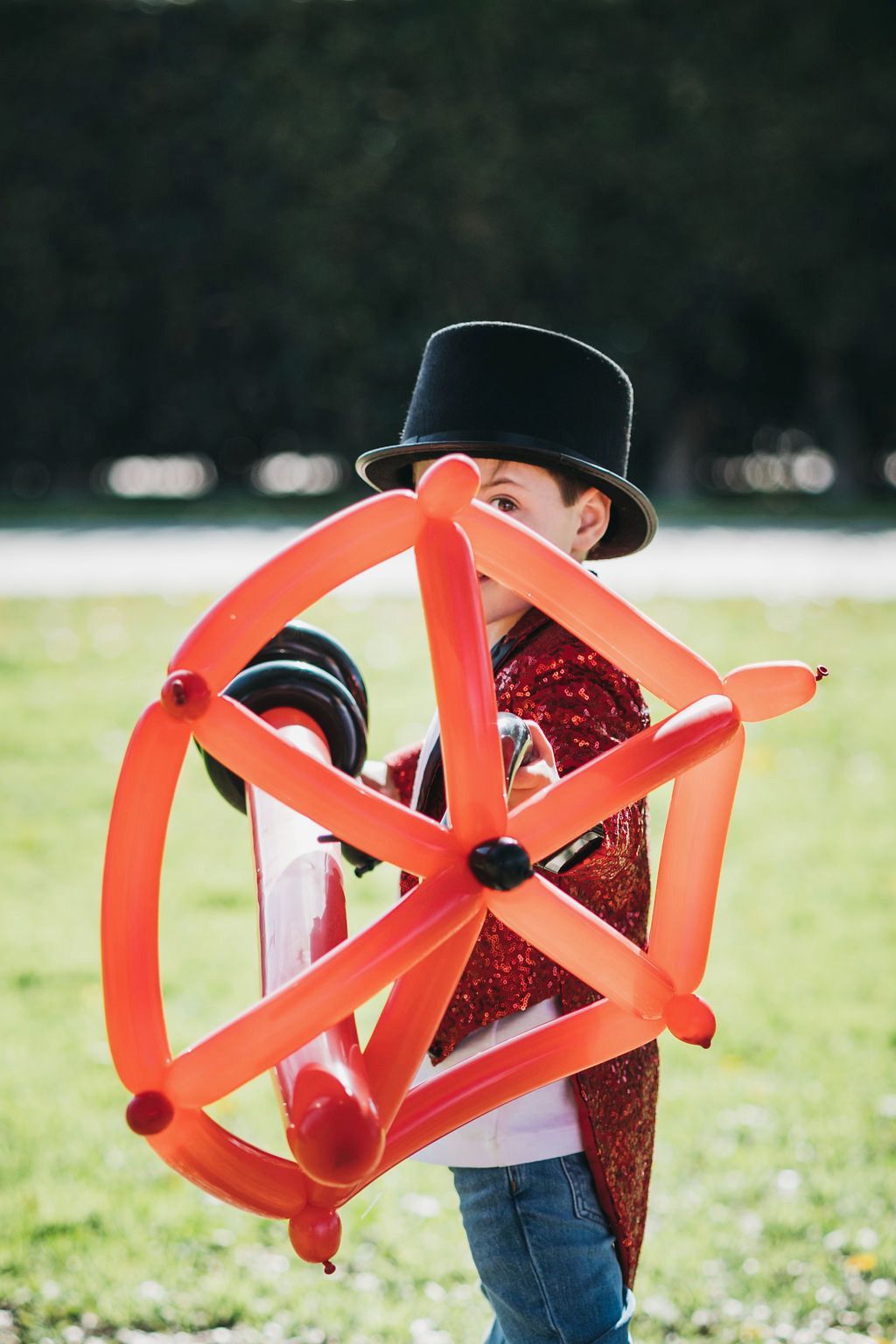 A young boy in a top hat is holding a steering wheel made of balloons.