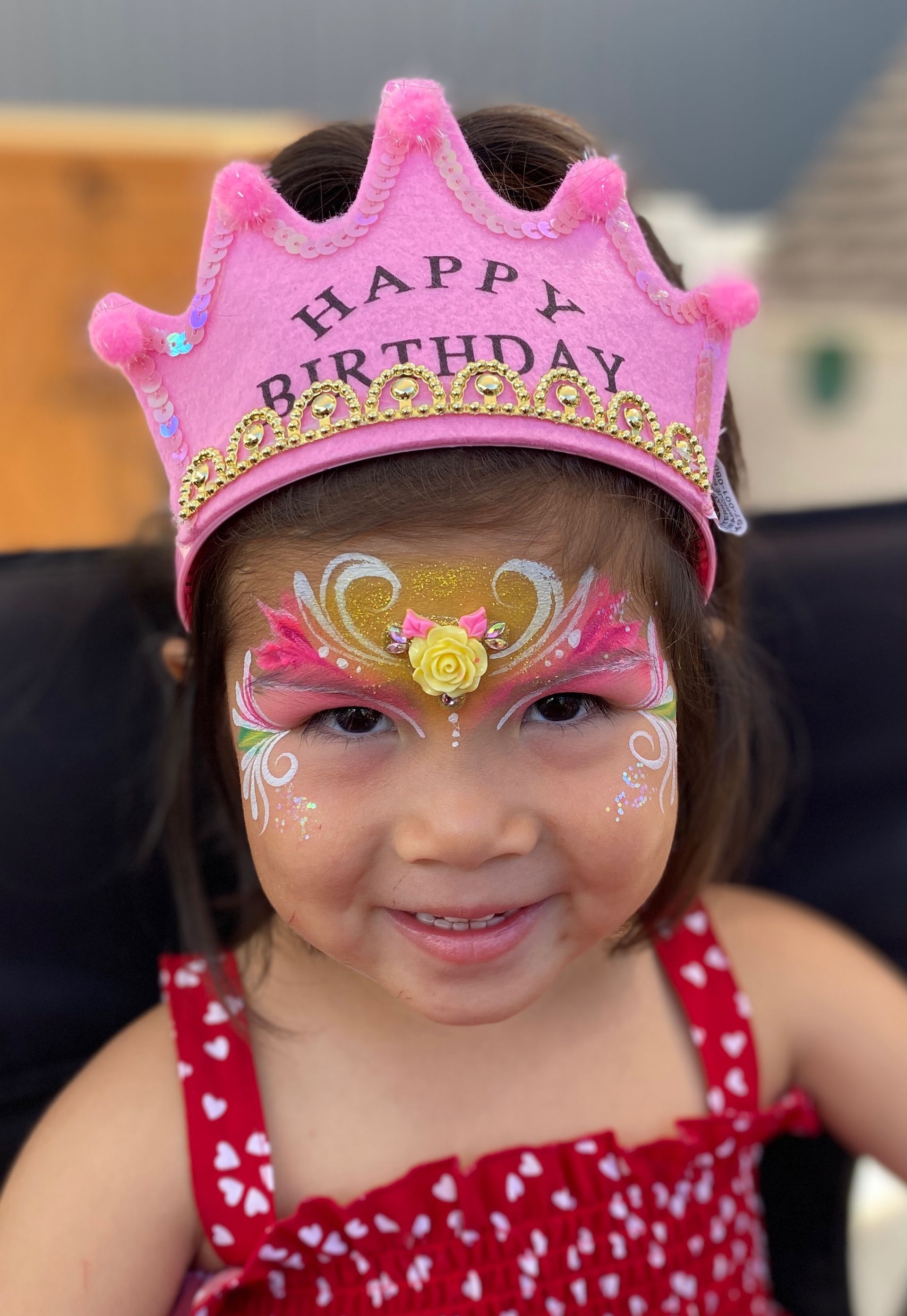 A little girl with her face painted and a pink crown on her head.