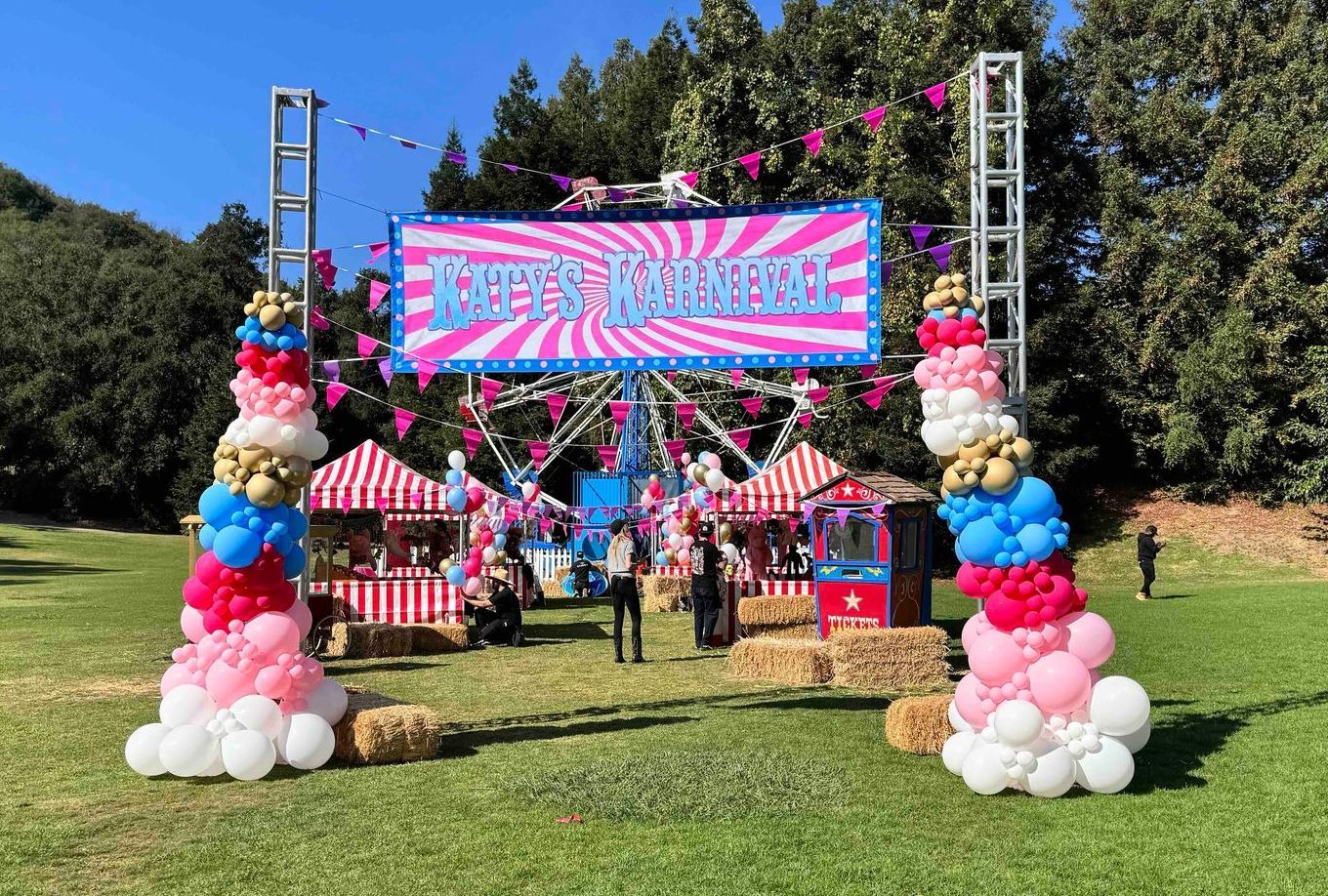 A carnival with a ferris wheel and balloons in a field.