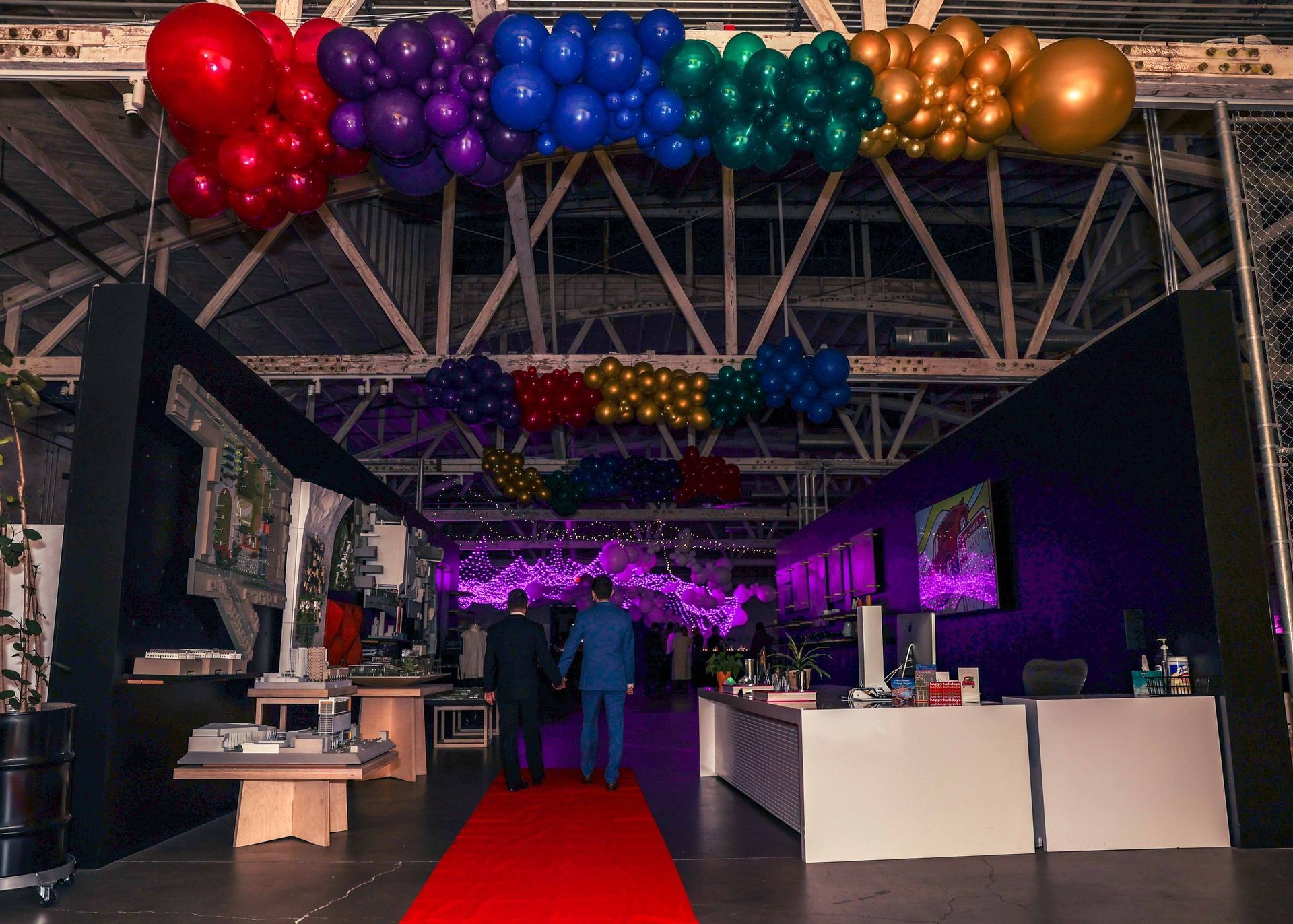 People are walking down a red carpet in a room with balloons hanging from the ceiling.