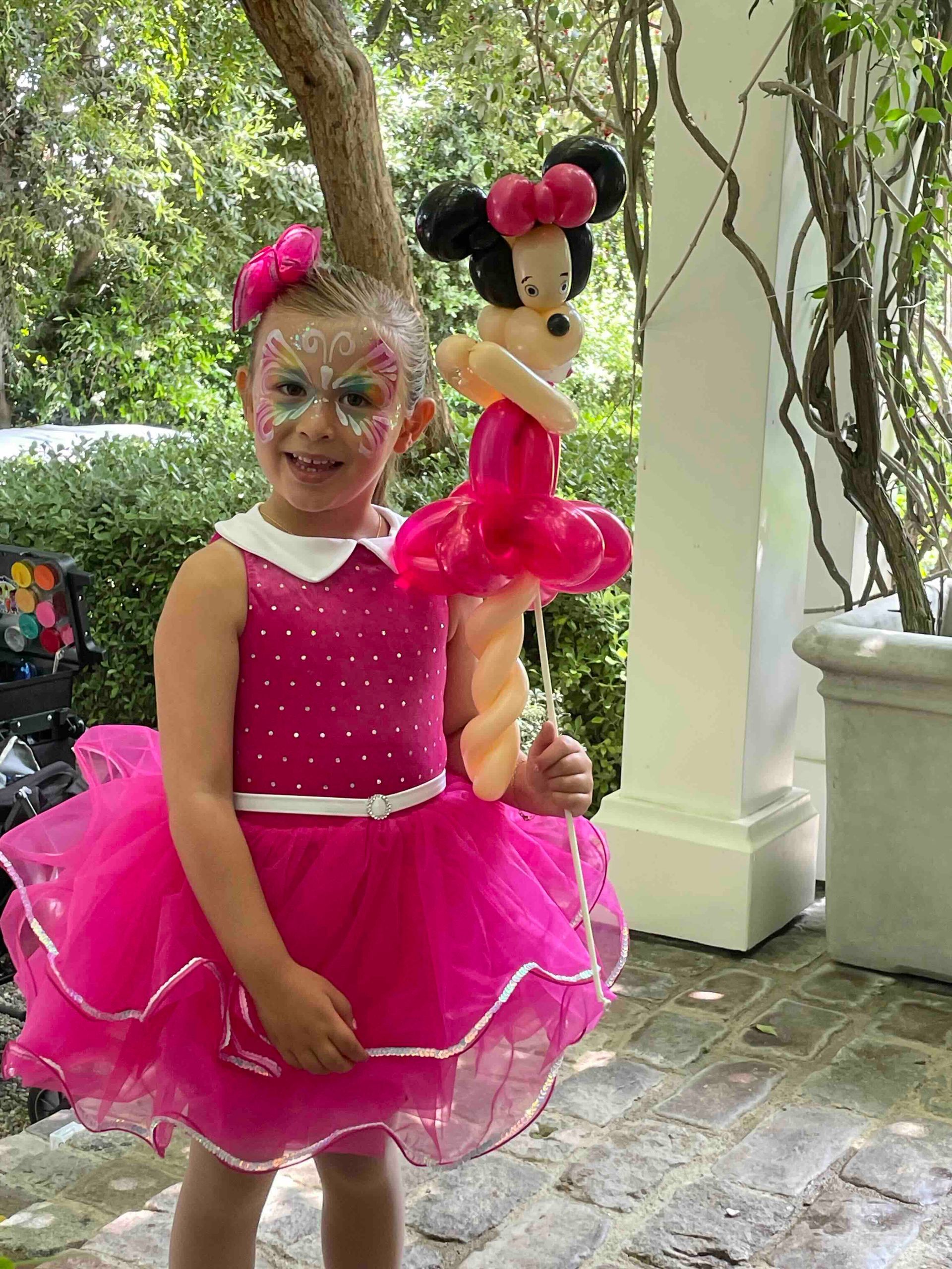 A little girl in a pink dress is holding a minnie mouse balloon.