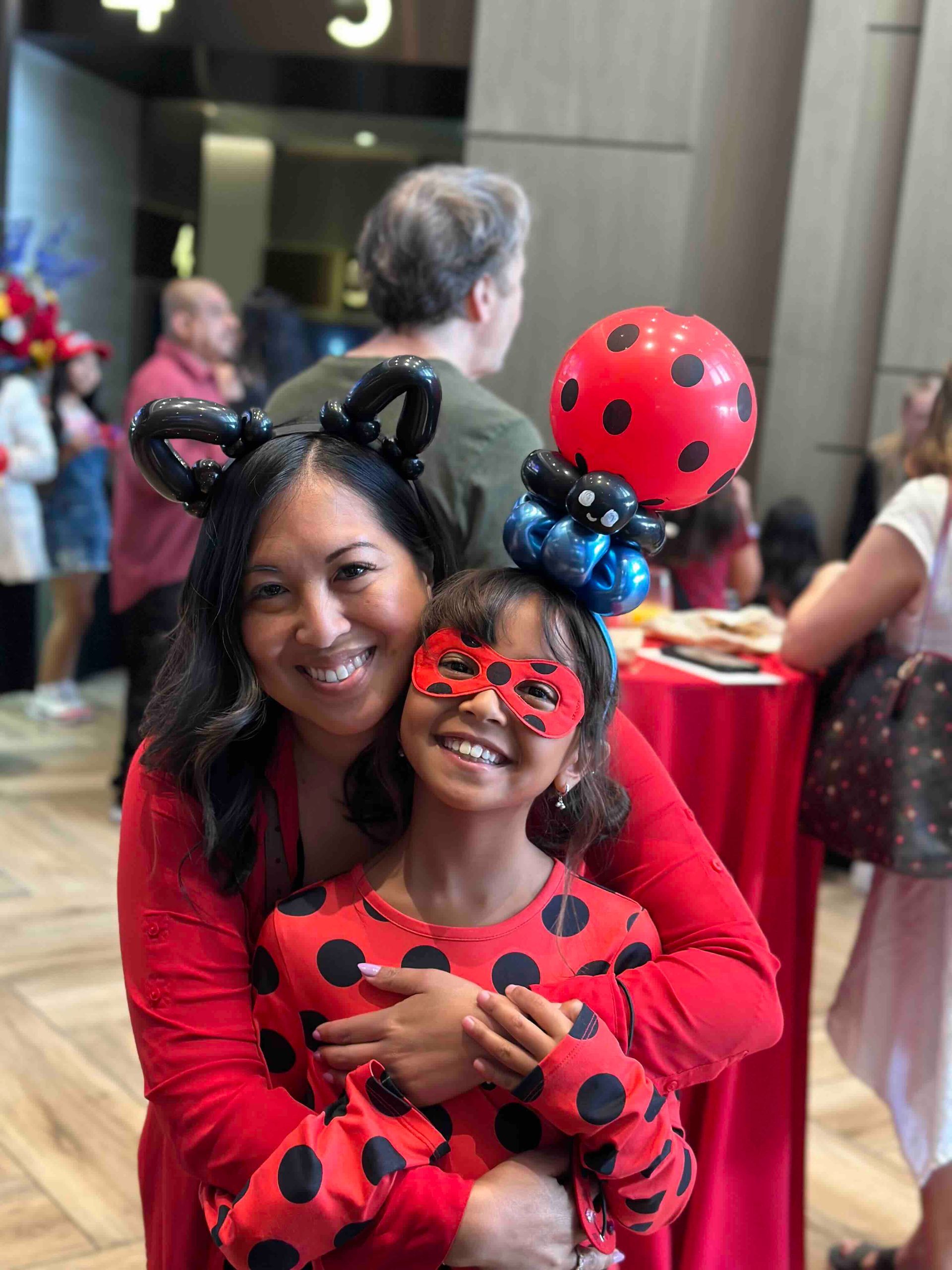 A woman is holding a little girl in a ladybug costume.