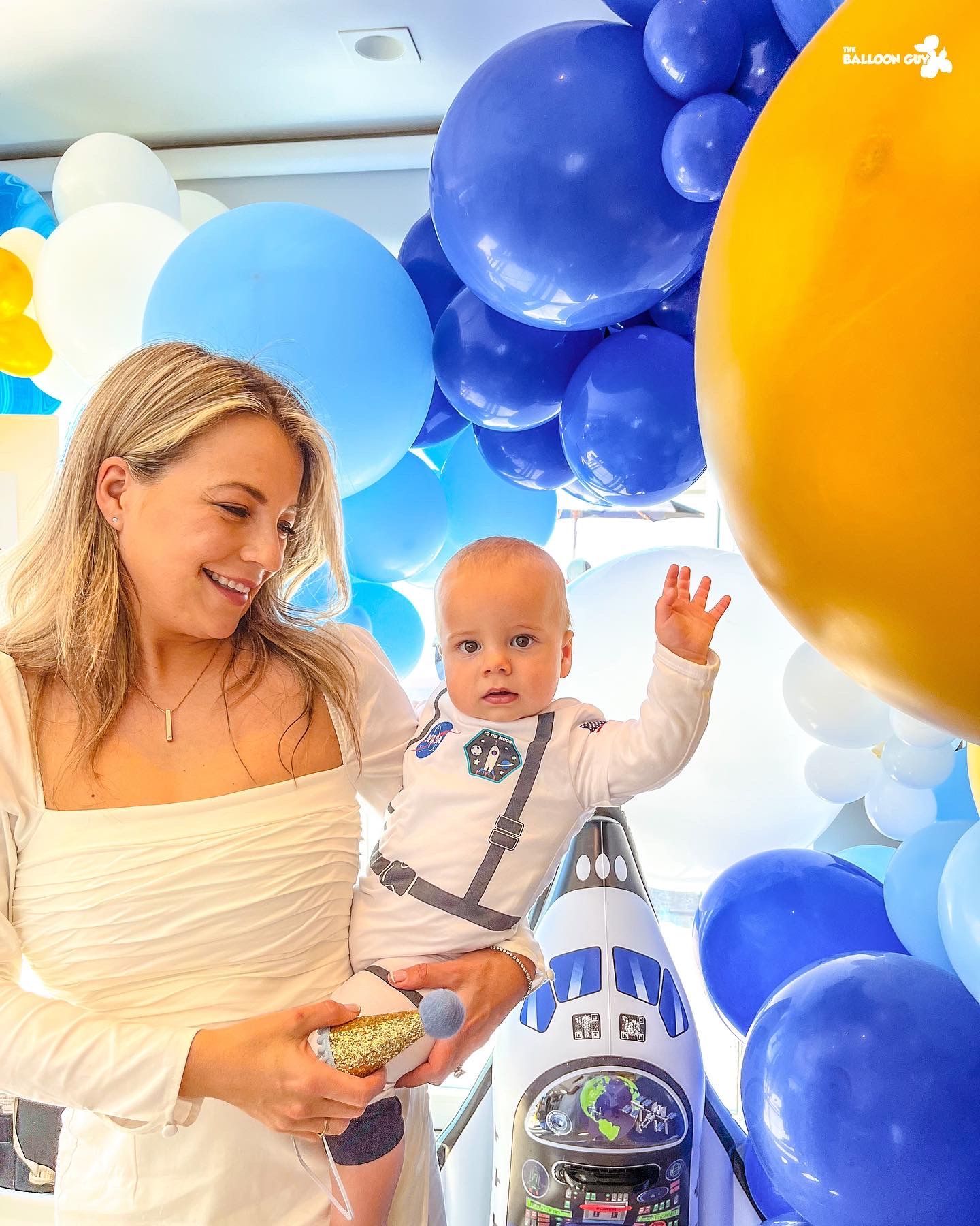 A woman is holding a baby in her arms in front of balloons.