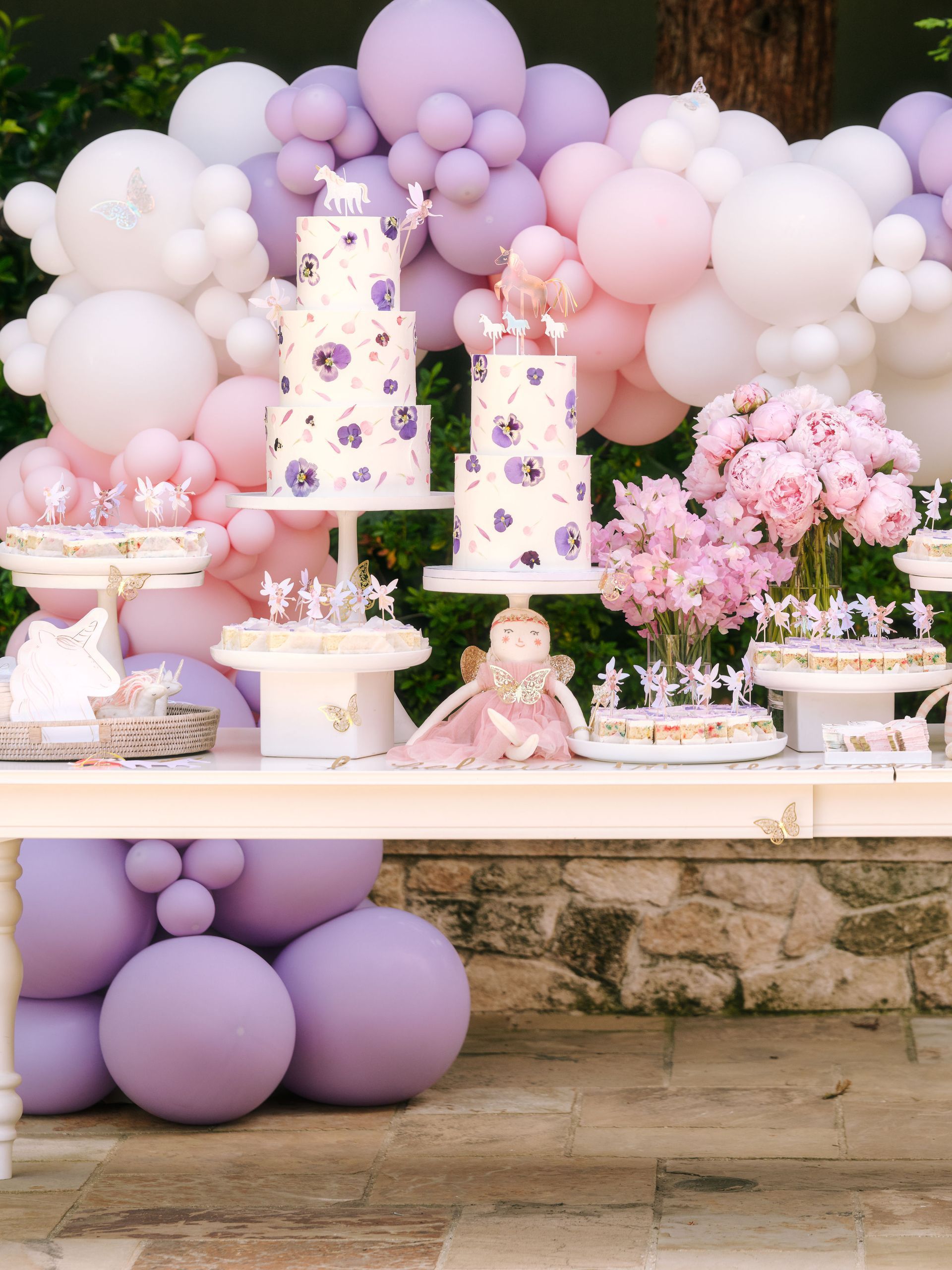 A table with purple and pink balloons and cakes on it