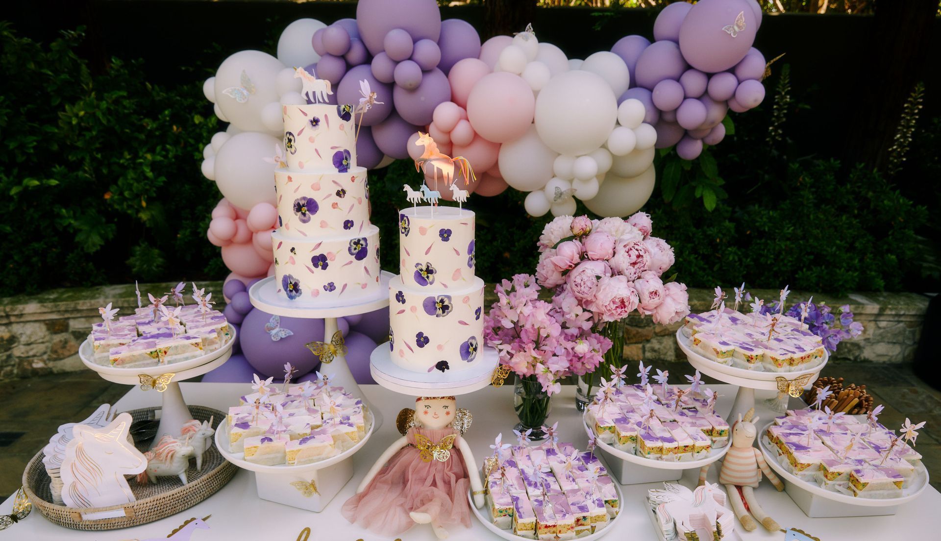 A table with a cake , cupcakes , and balloons on it.