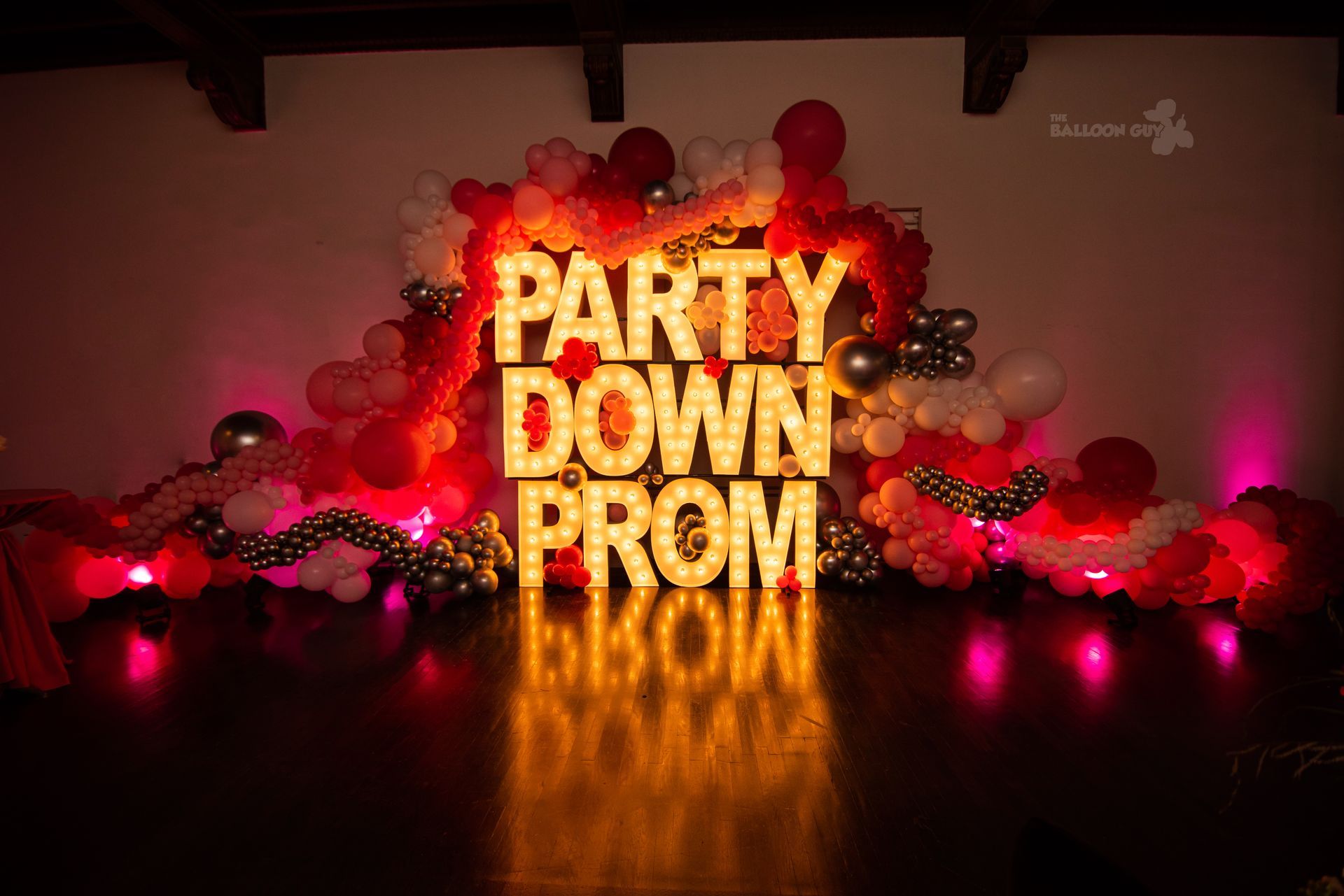 A sign that says `` party down prom '' is surrounded by balloons and lights.
