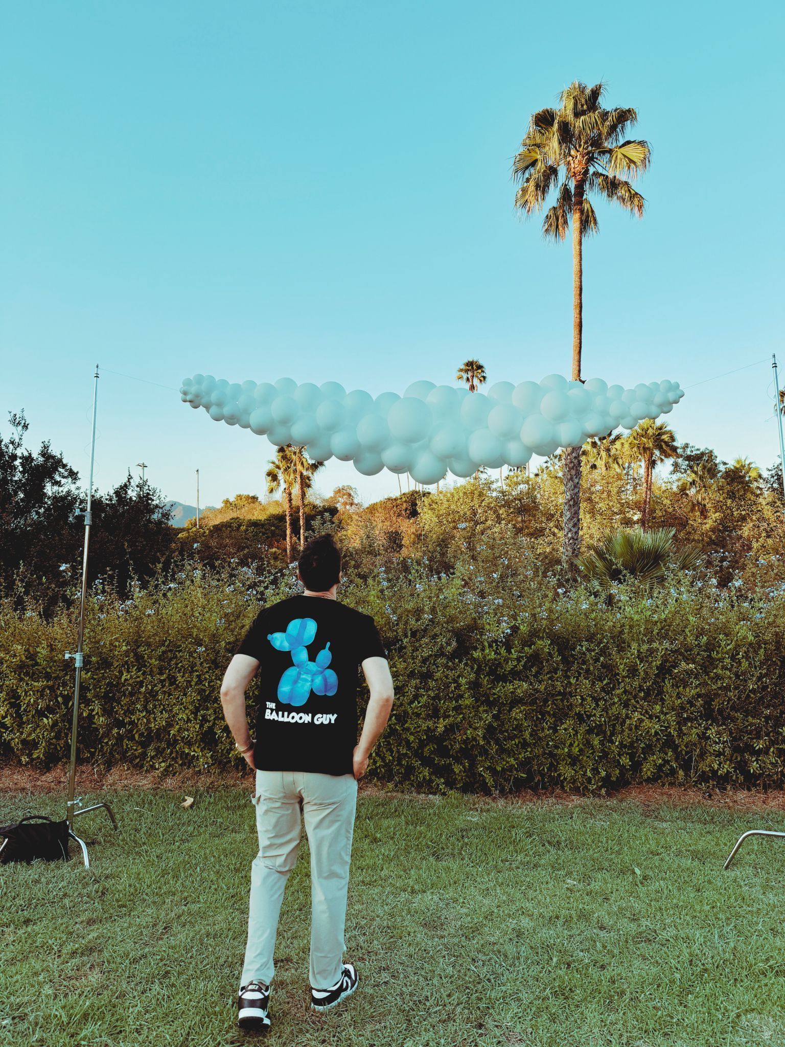 A man in a black shirt is standing in front of a cloud of balloons.