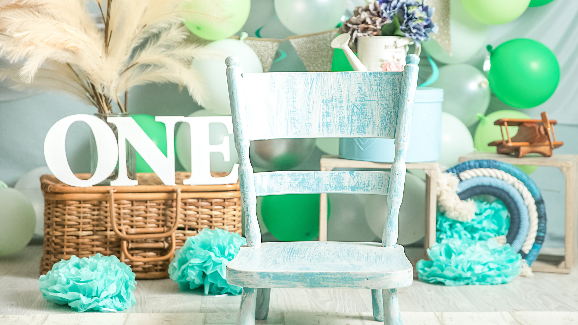A baby 's first birthday is being celebrated with balloons and a chair.