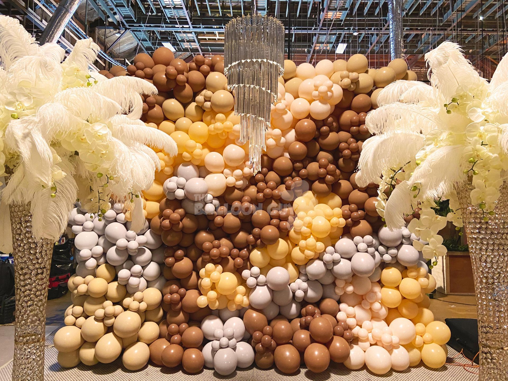 A wall made of balloons and flowers with a chandelier in the background.