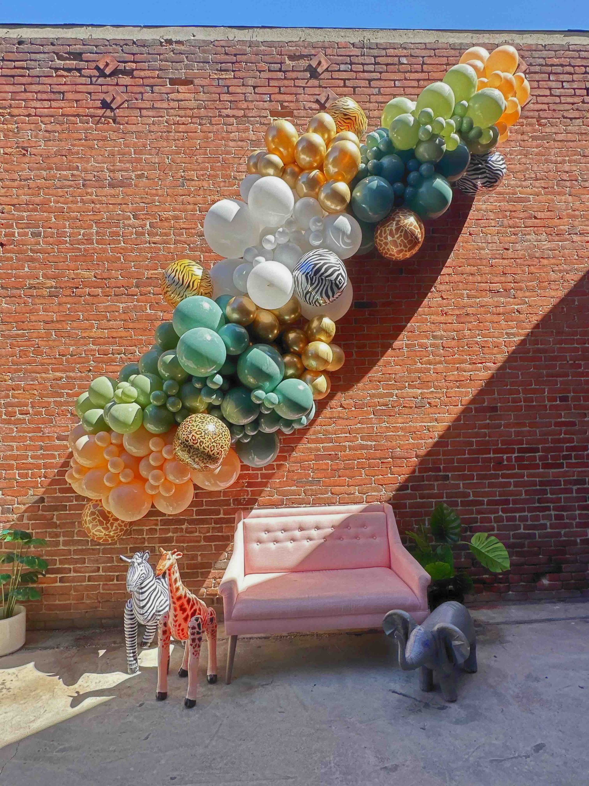 A pink couch is sitting in front of a brick wall with balloons hanging from it.