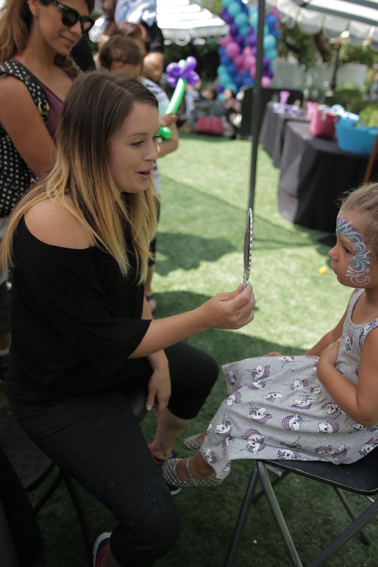 A woman is sitting next to a little girl with her face painted.