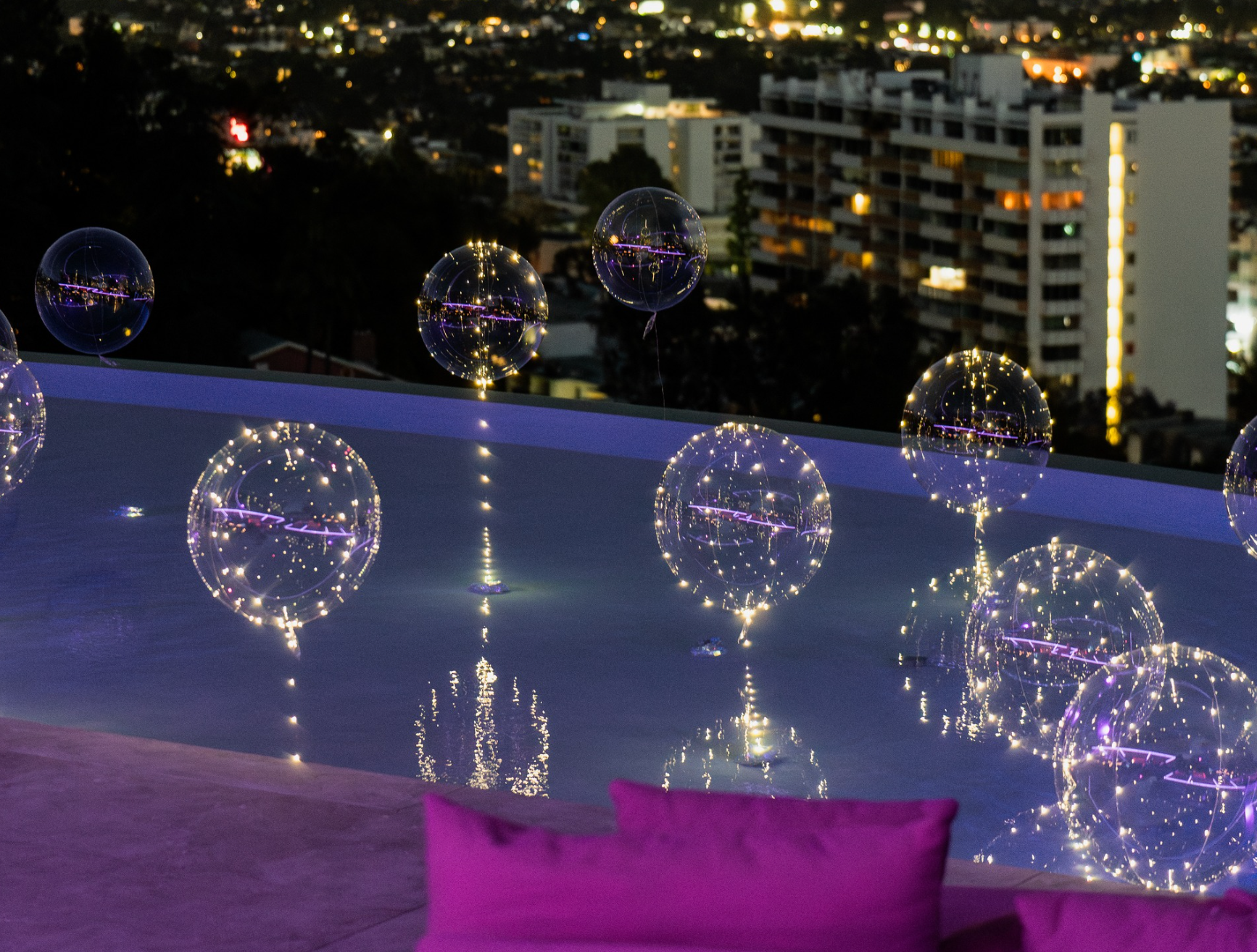 A swimming pool is decorated with balloons and lights at night