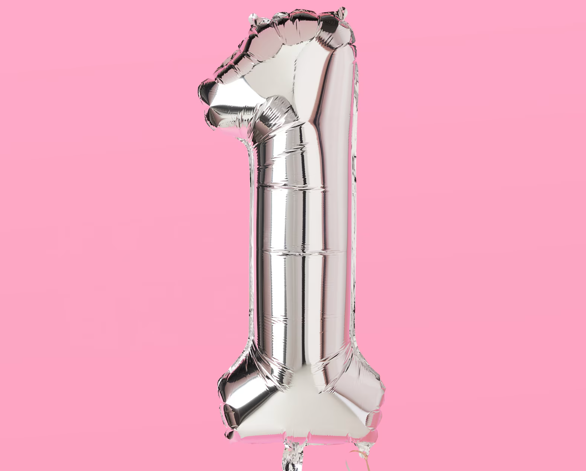 A silver balloon in the shape of the number one on a pink background.