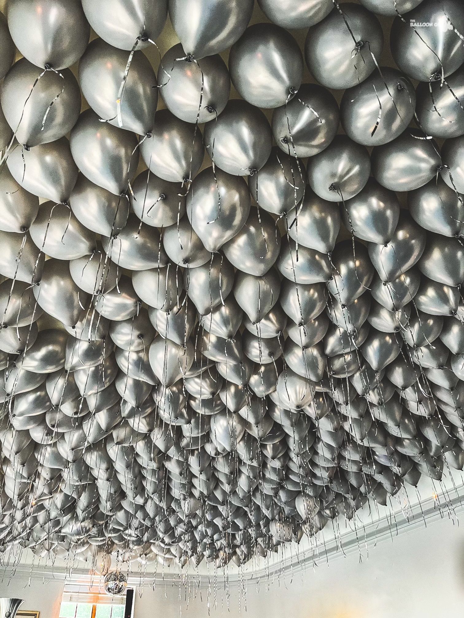 A bunch of silver balloons are hanging from the ceiling.