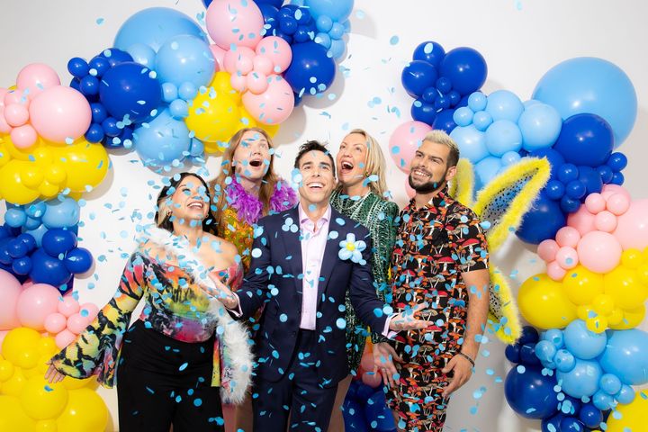 A group of people are standing in front of a wall of balloons and confetti.