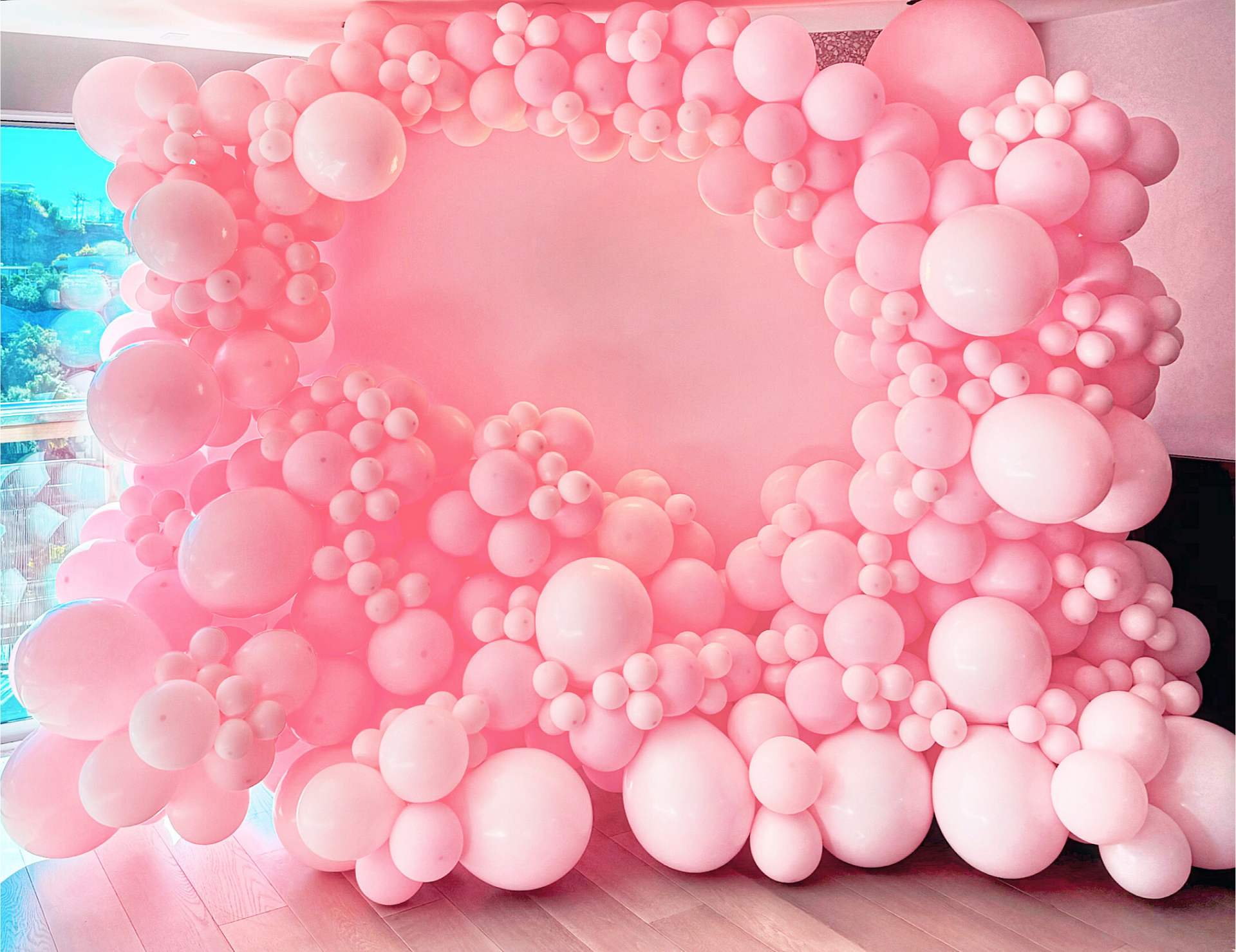 A wall of pink balloons on a wooden floor.