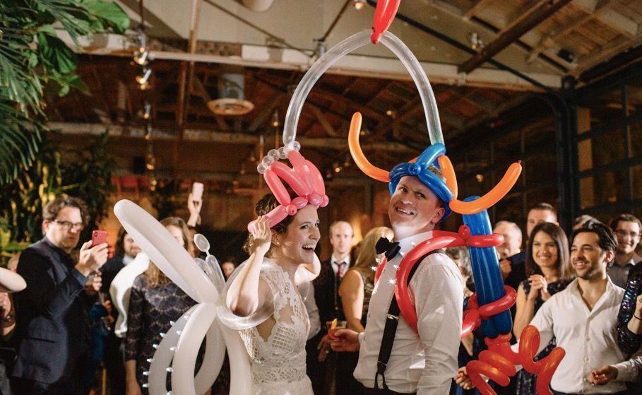 A bride and groom are holding balloons on their heads at a wedding reception.