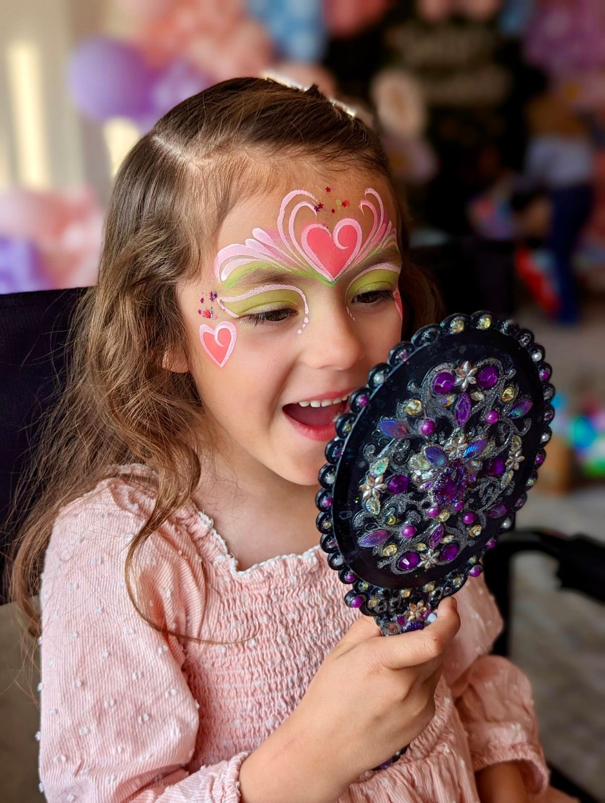 little girl looking in a mirror with her face painted with a heart