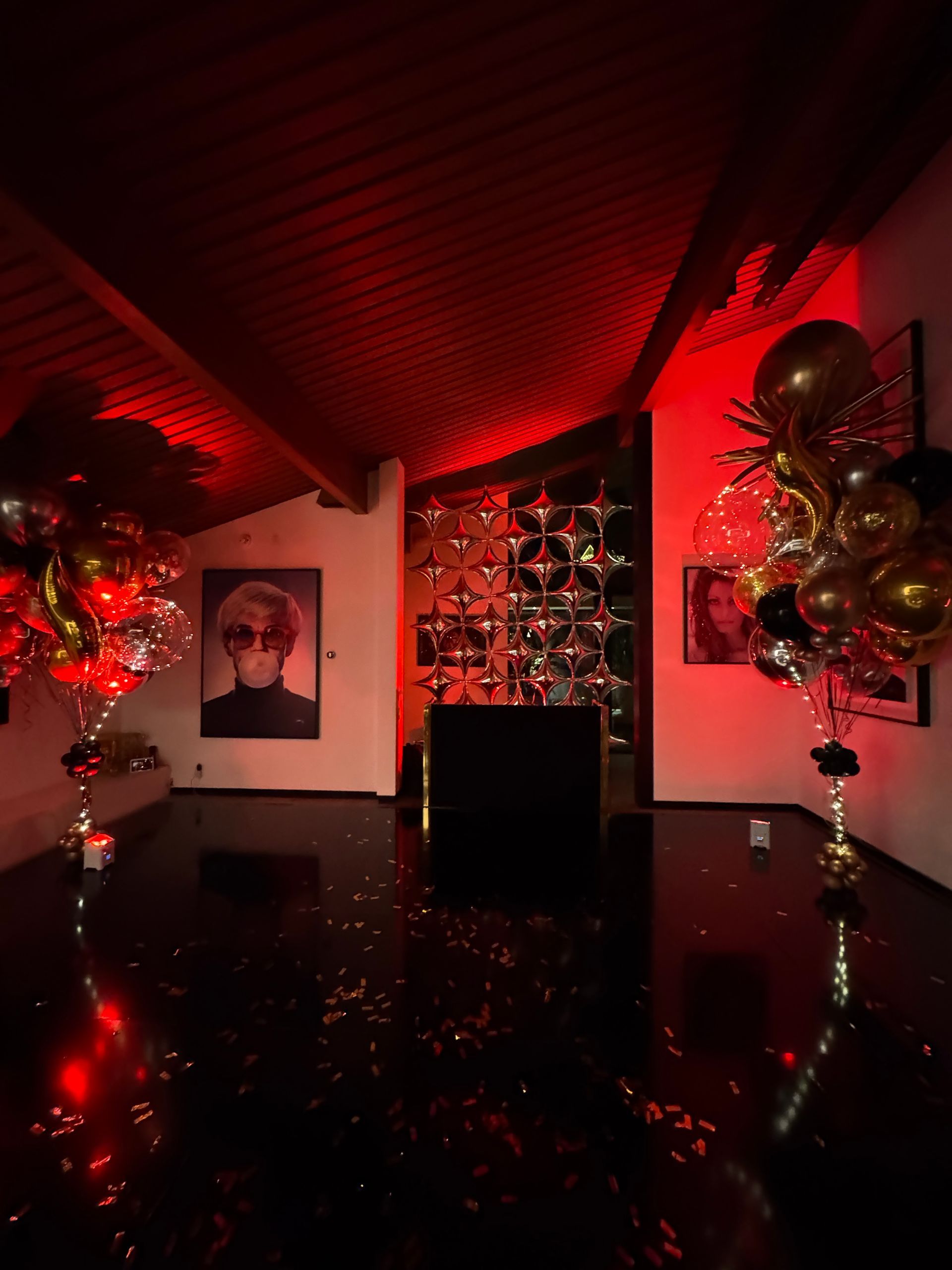 A room with balloons and confetti on the floor and a red light on the ceiling.