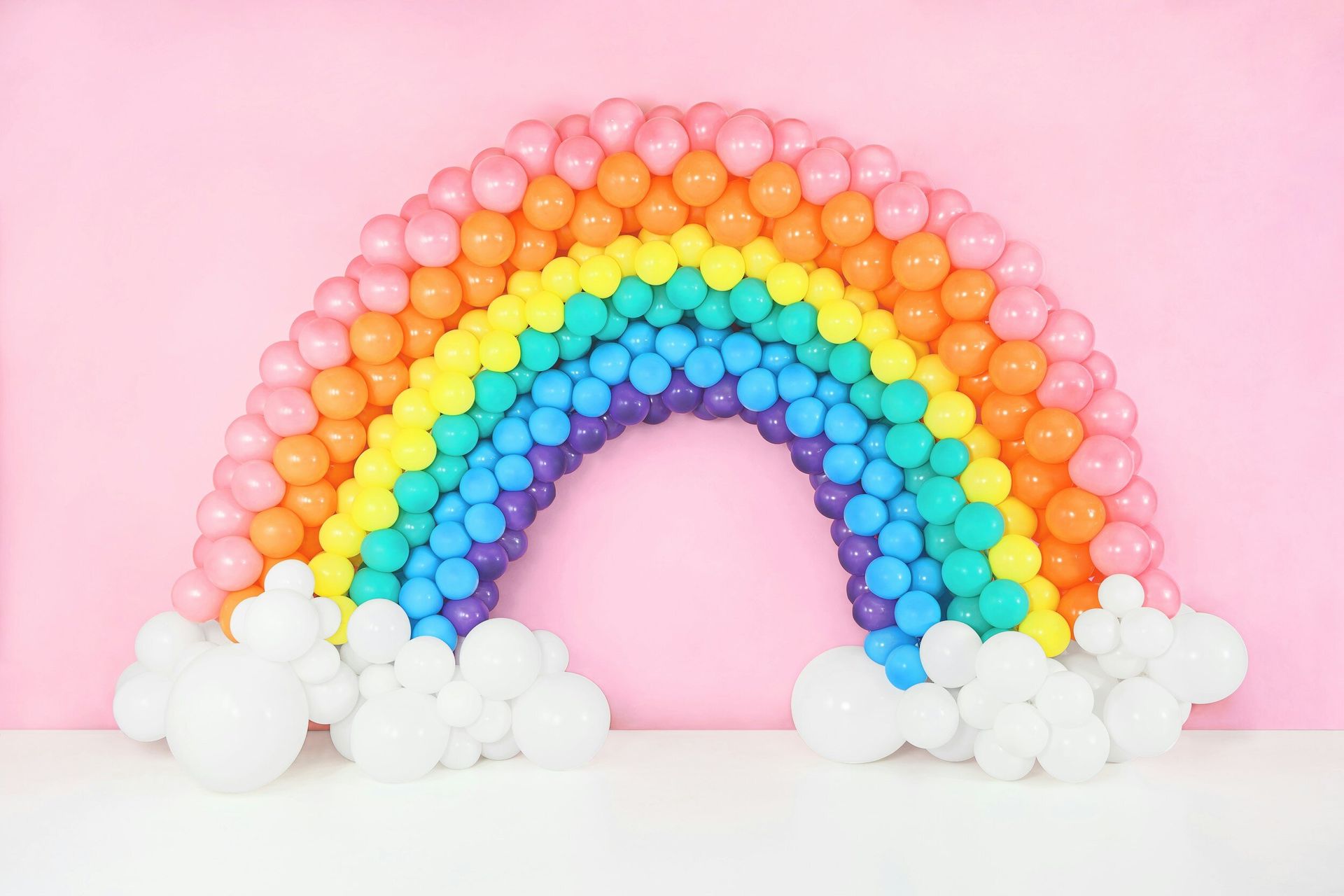 A rainbow made of balloons on a pink background.