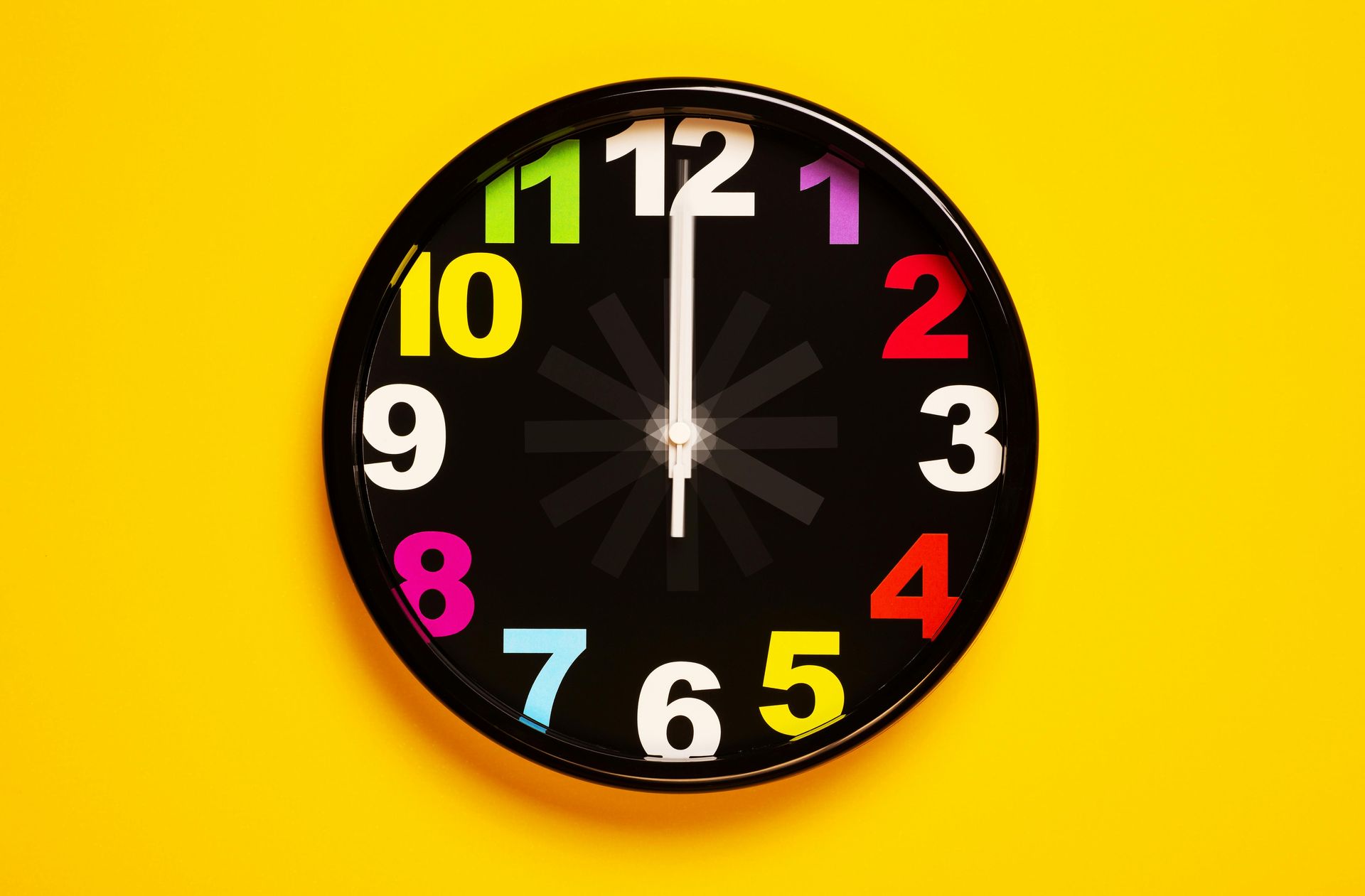 A black clock with colorful numbers on a yellow background.