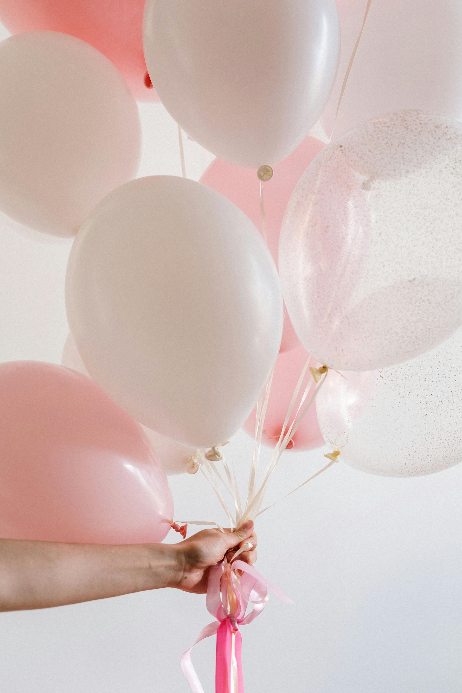 A person is holding a bunch of pink and white balloons.