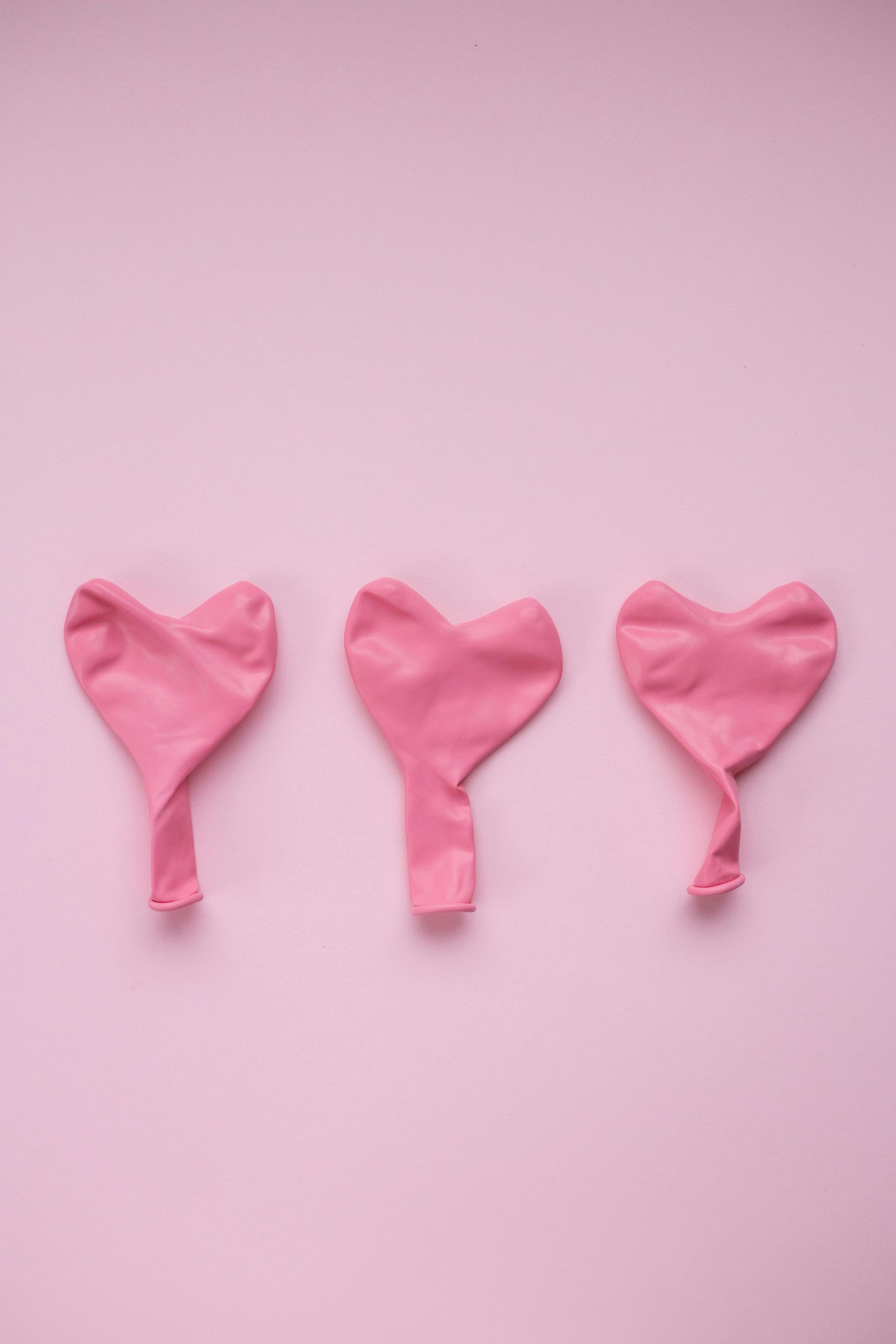 Three pink balloons in the shape of a heart on a pink background.