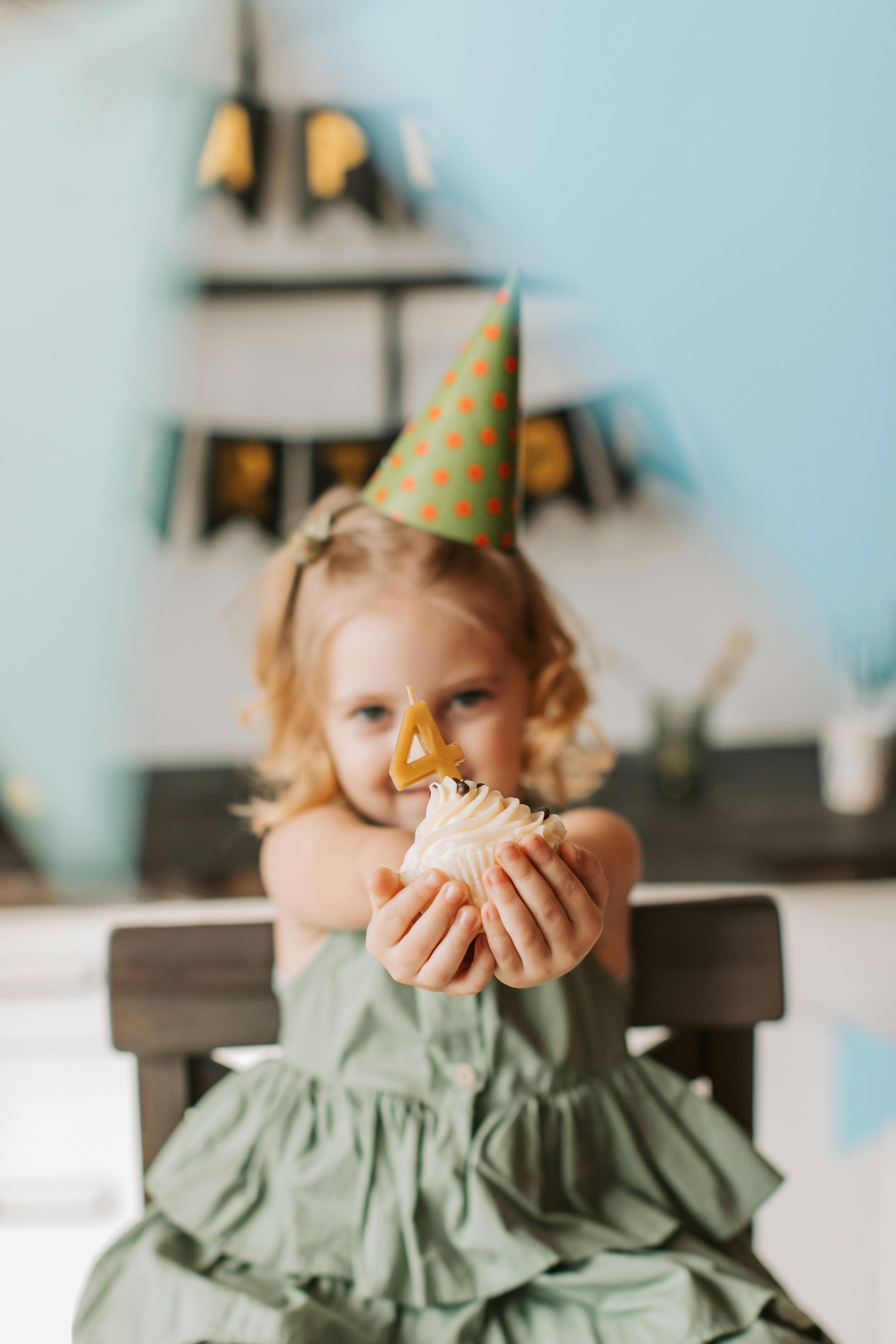 A little girl wearing a party hat is holding a cupcake in her hands.