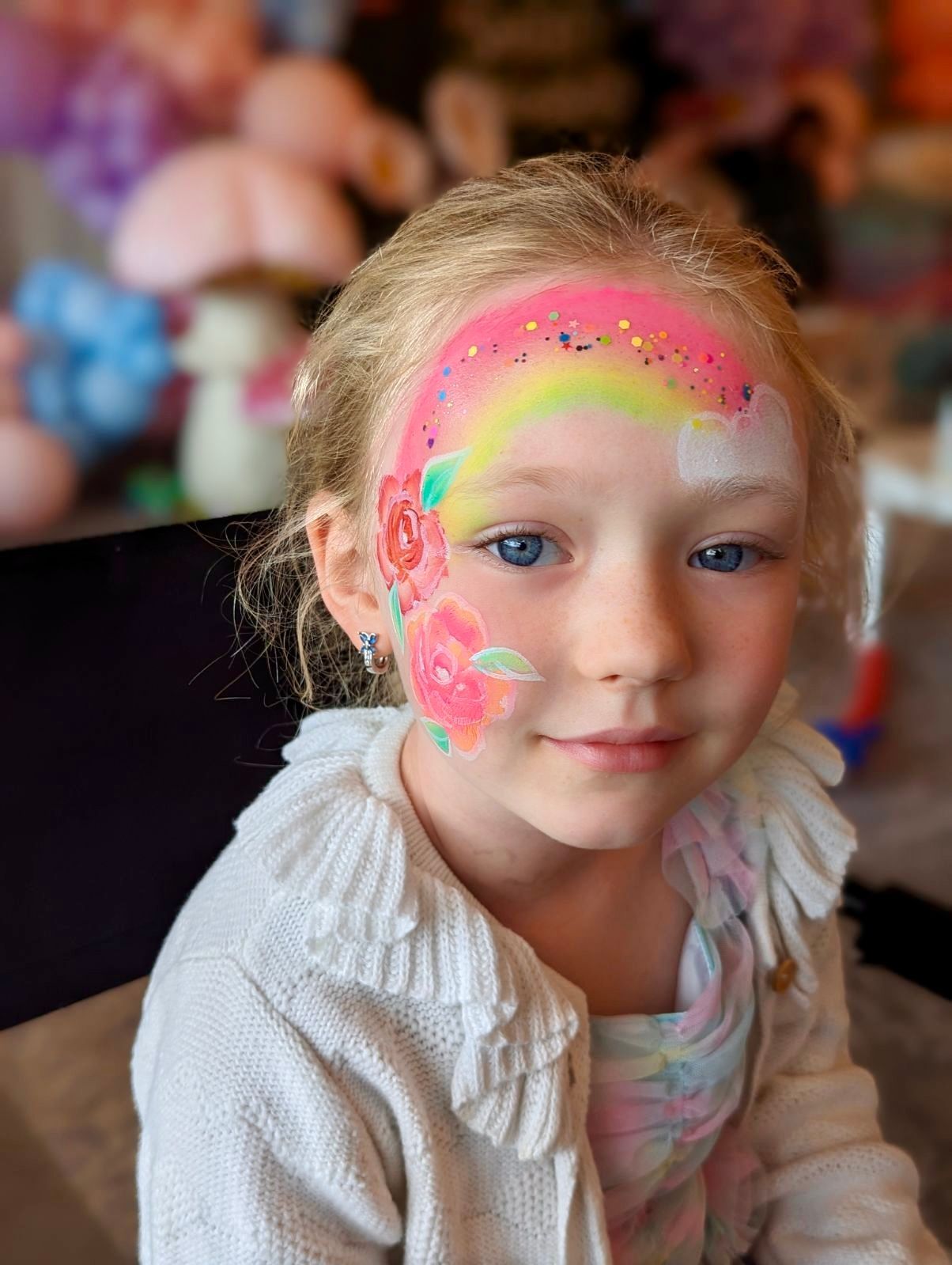 A little girl with a rainbow and roses painted on her face.