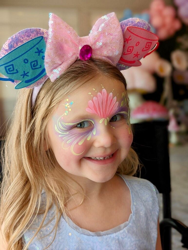 A little girl with face paint and ears on her head.