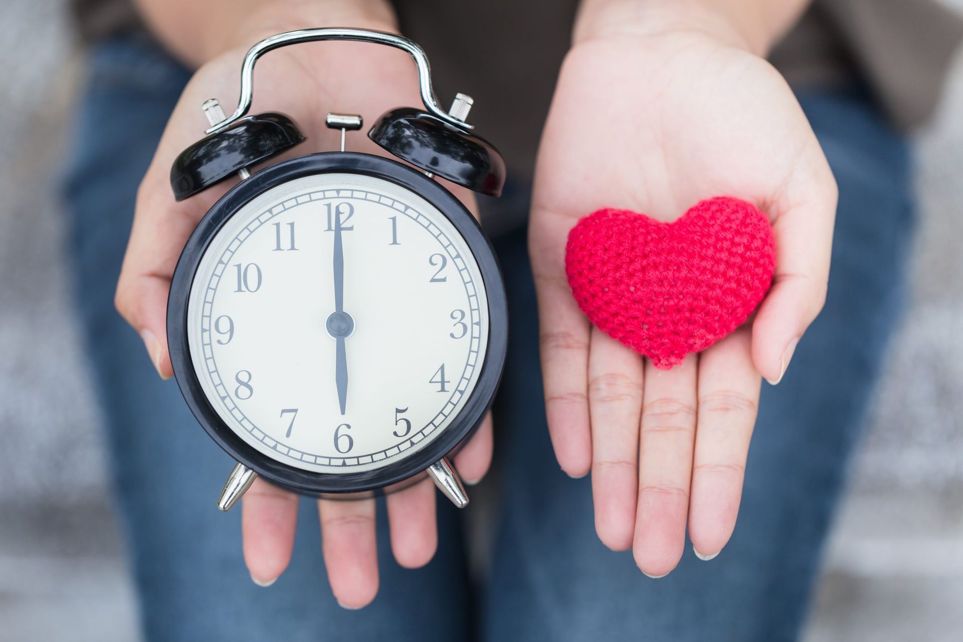 A person is holding a clock and a heart in their hands.