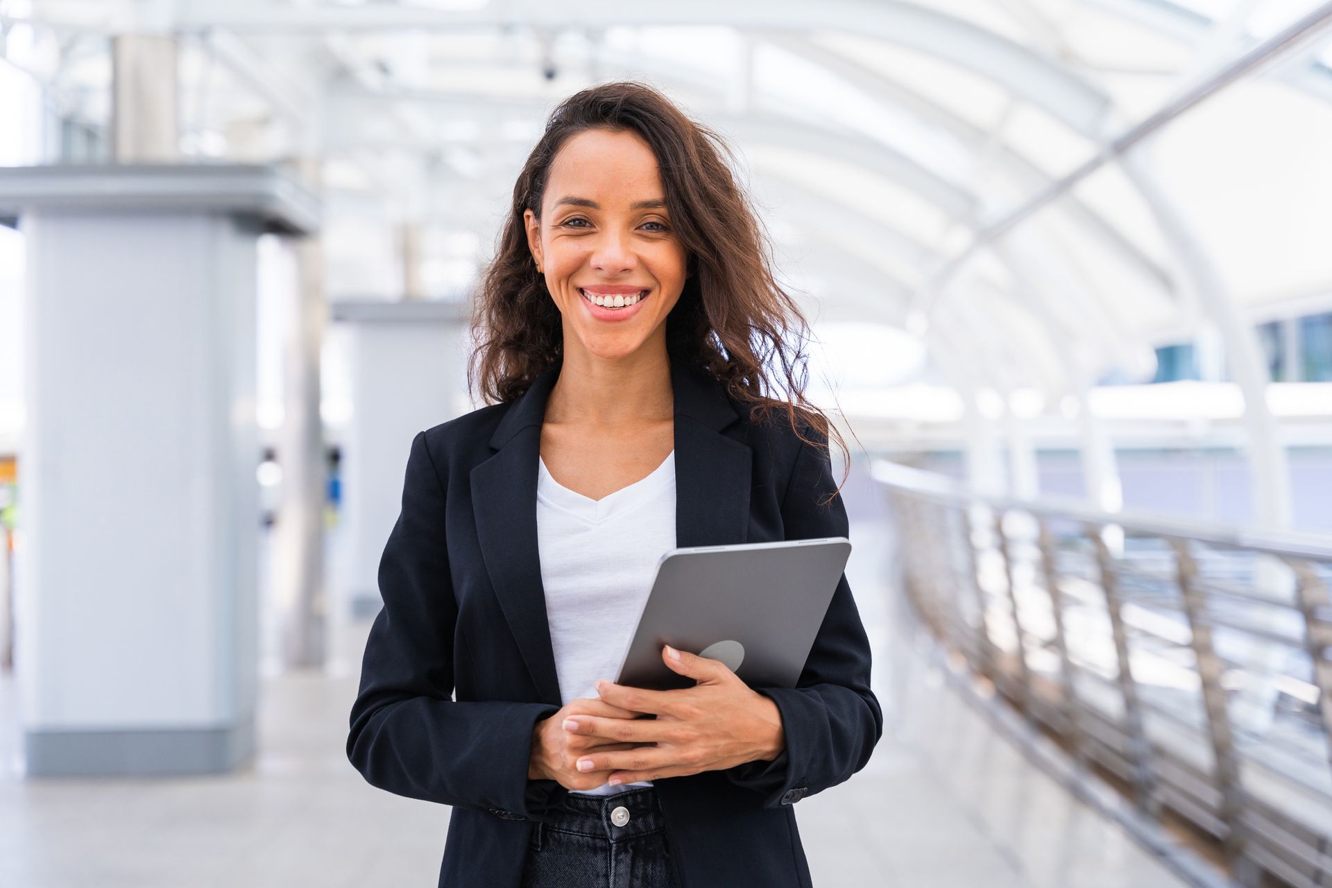 A woman in a suit is holding a tablet and smiling.