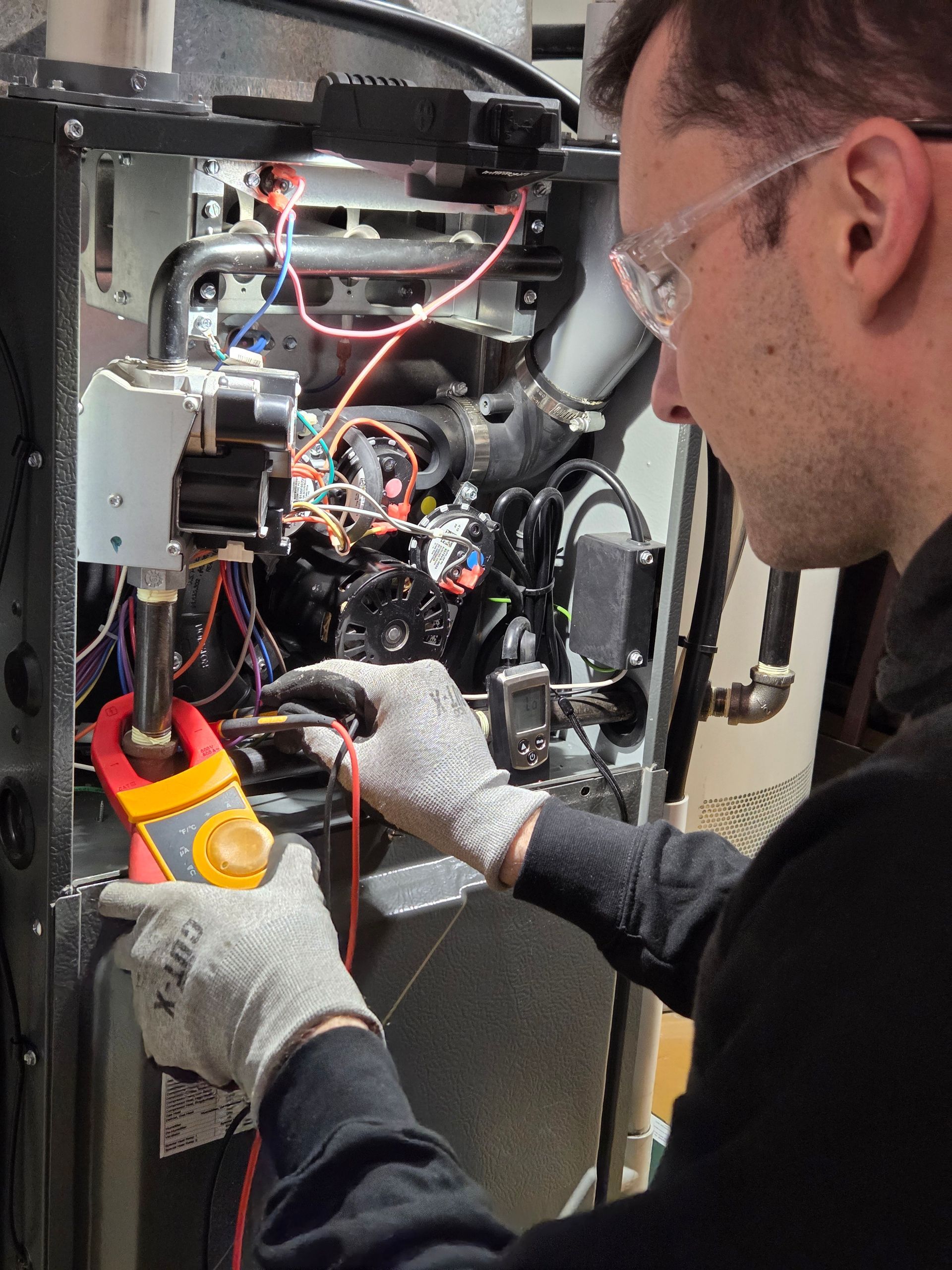 Person in safety glasses and gloves using a multimeter to inspect the interior of a heating unit.