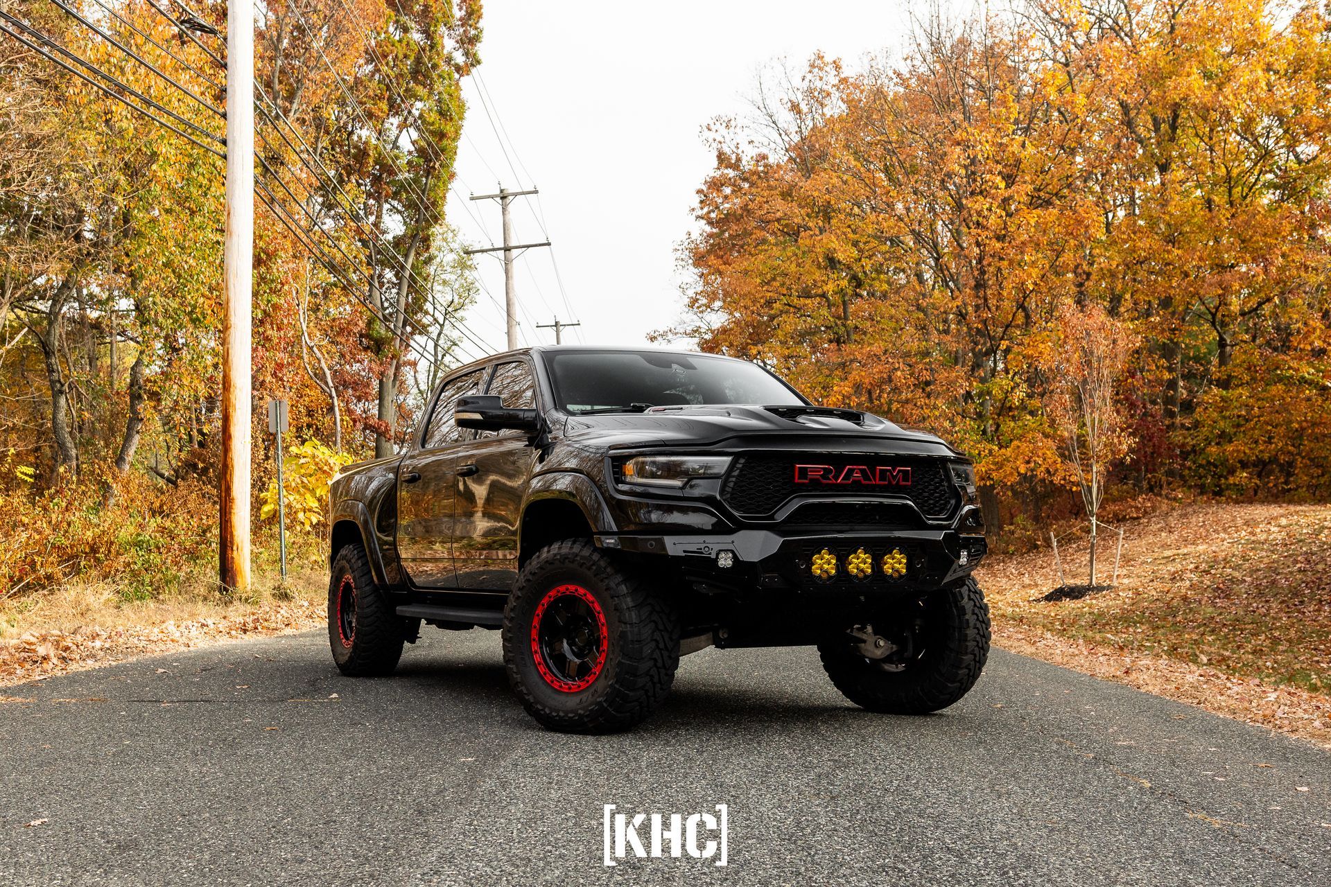 Black pickup truck with red-accented wheels on a paved road, fall foliage in the background.