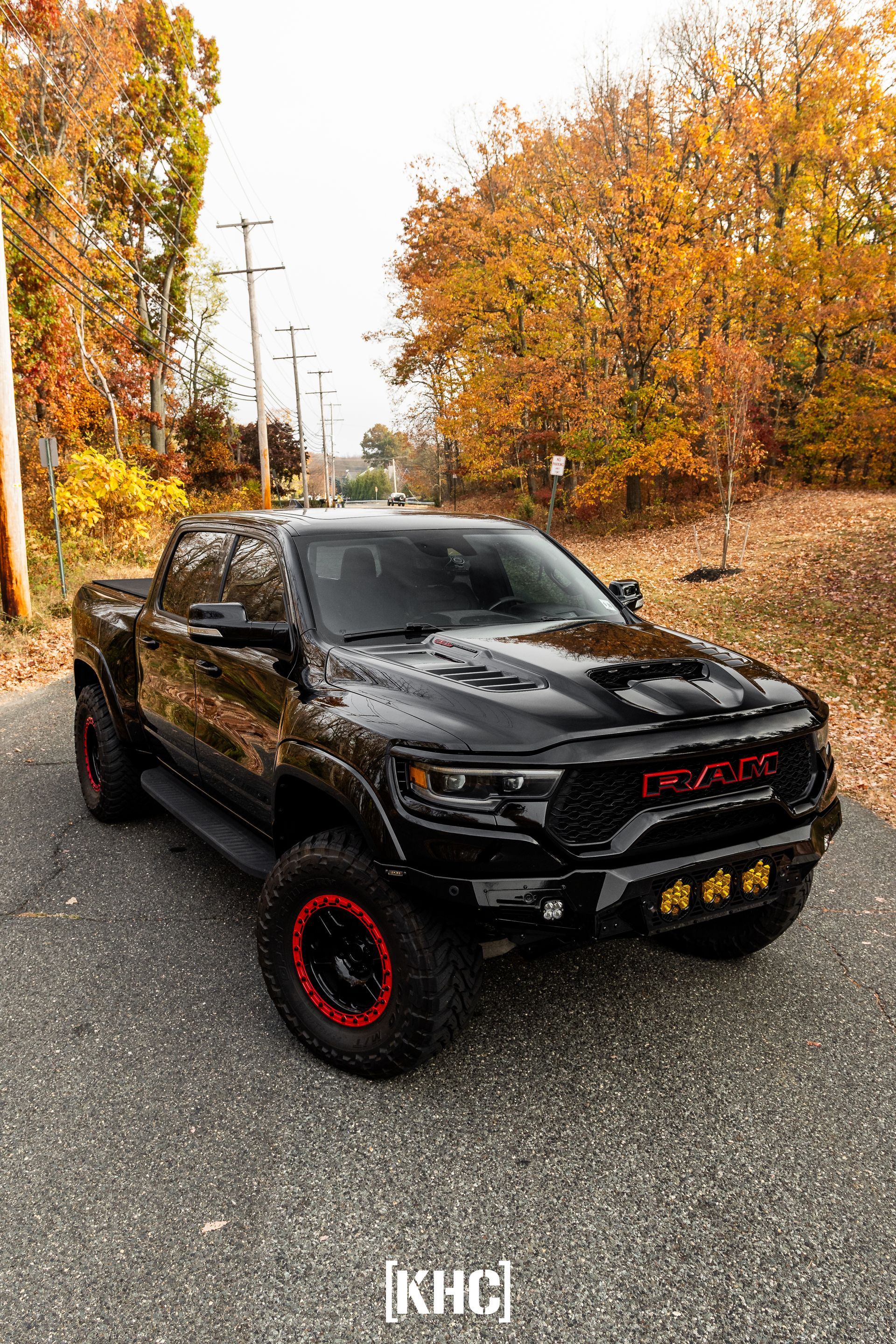 Black Ram TRX truck with red accents, parked on a road lined with trees displaying autumn colors.