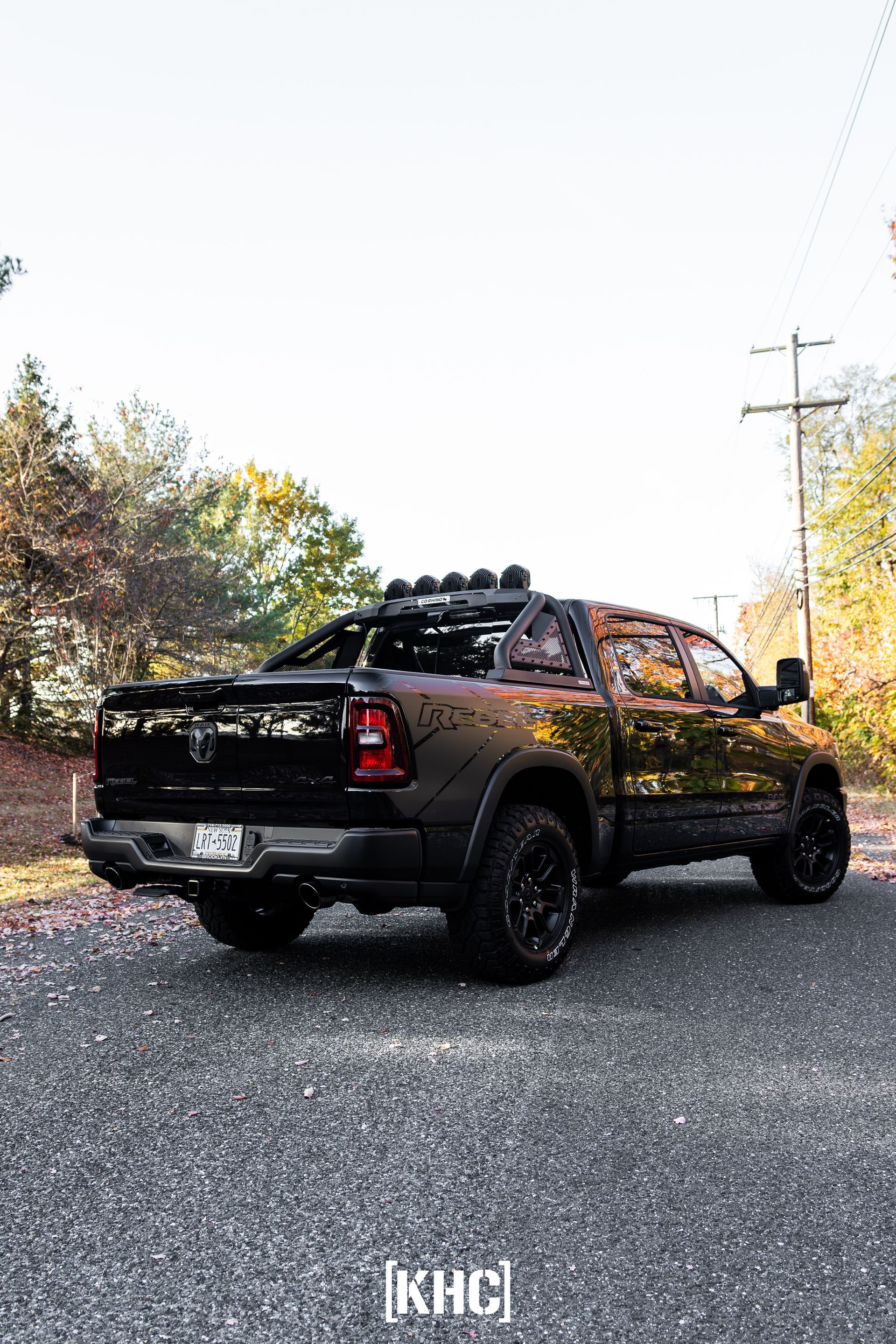 Black Ram pickup truck parked on gravel road with forested background.