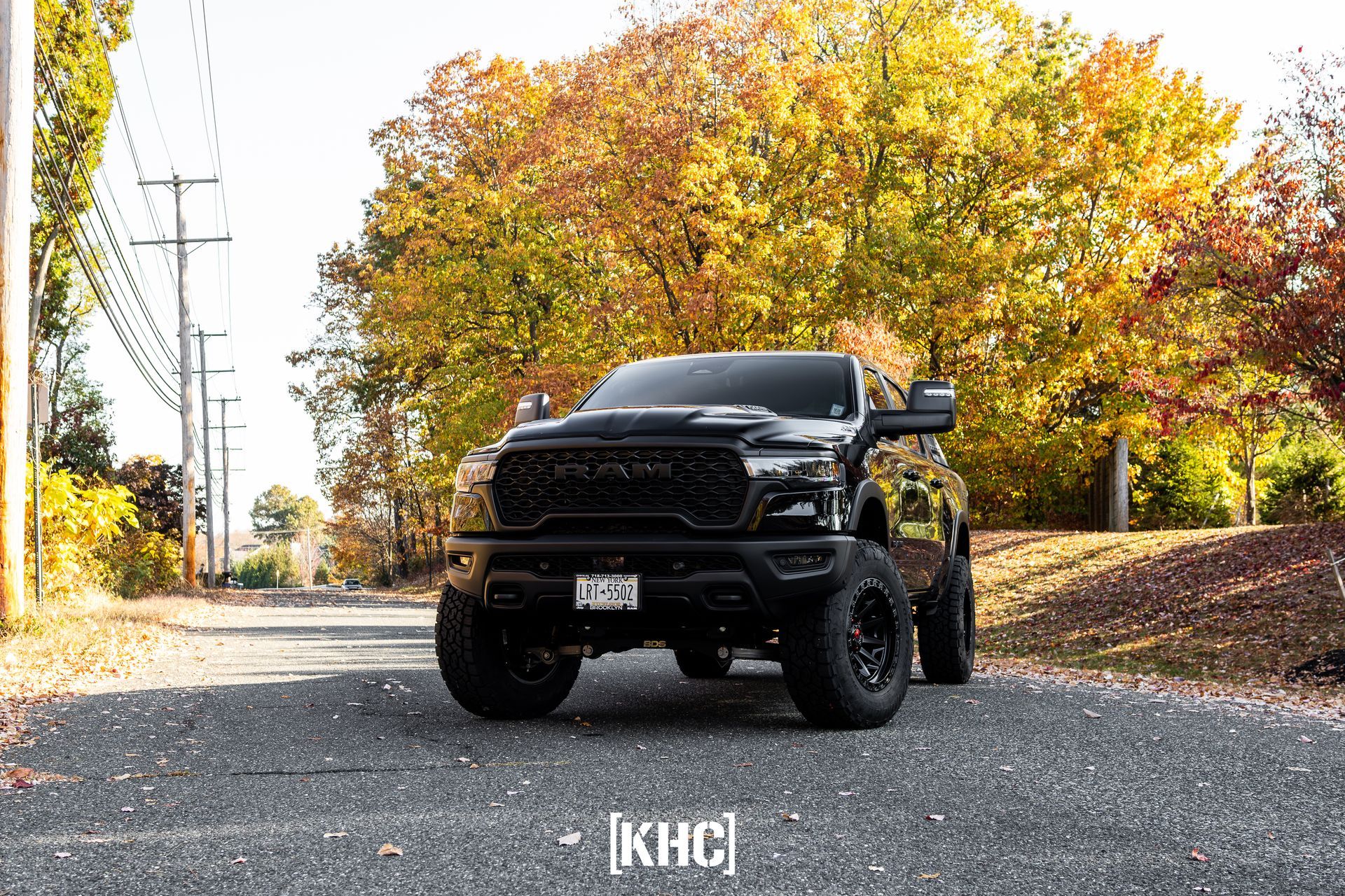 Black Ram truck on a road, fall foliage in the background.