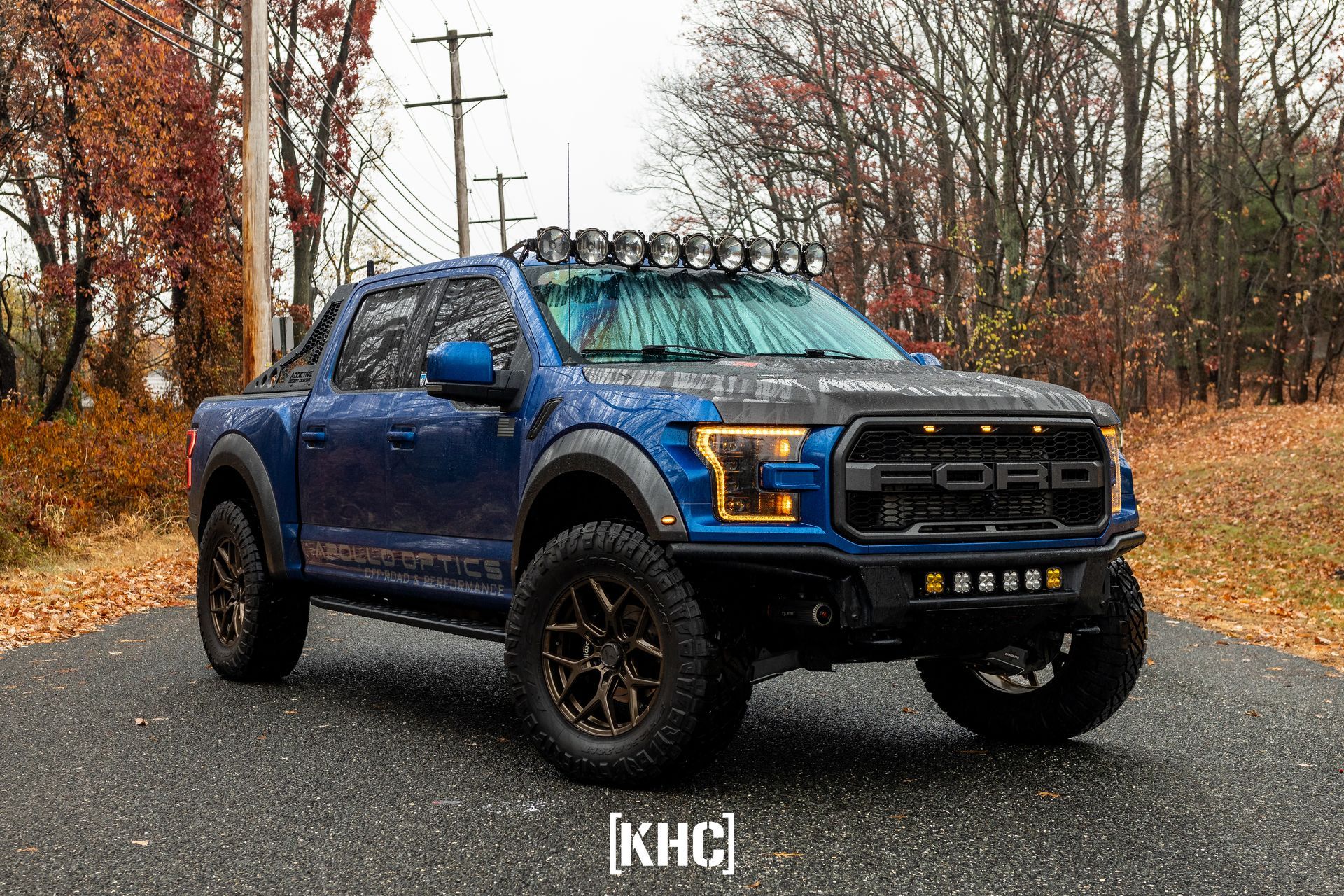 Gray Ford Raptor truck, front view, illuminated headlights and auxiliary lights, parked at night.