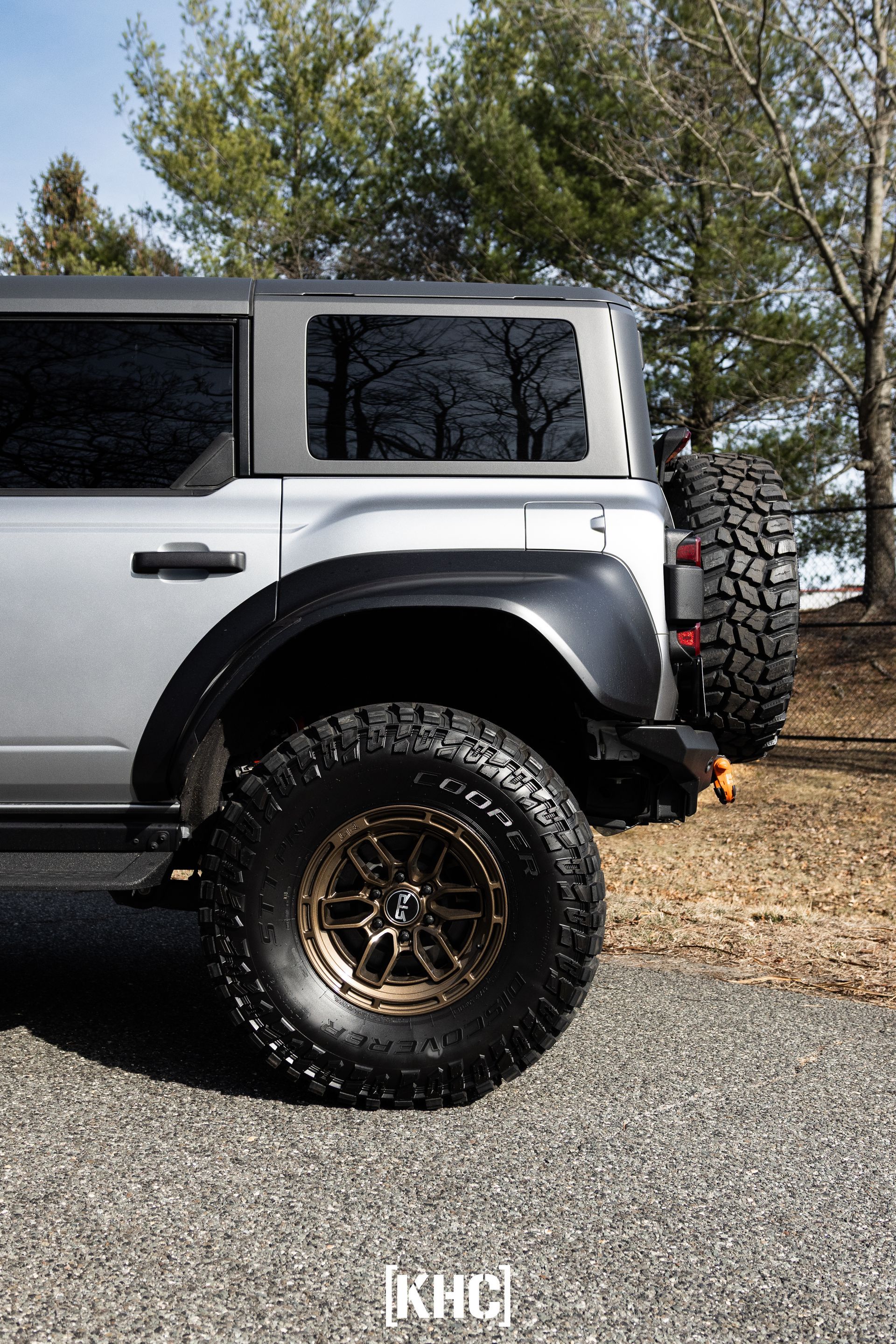 Silver Bronco SUV with black fender flares and bronze wheels, parked outdoors.