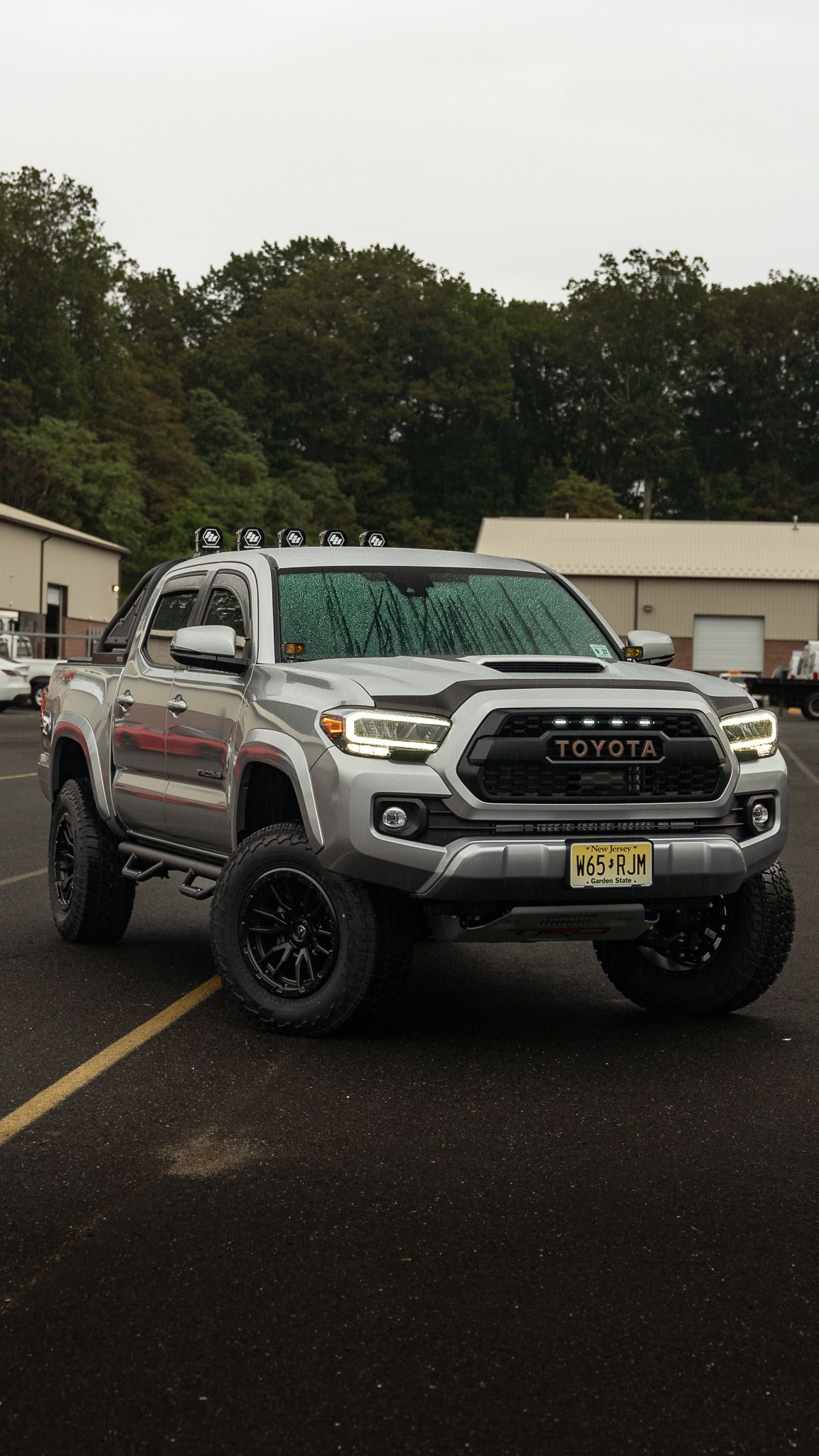 Silver Toyota Tacoma truck with black wheels and grill parked on asphalt.