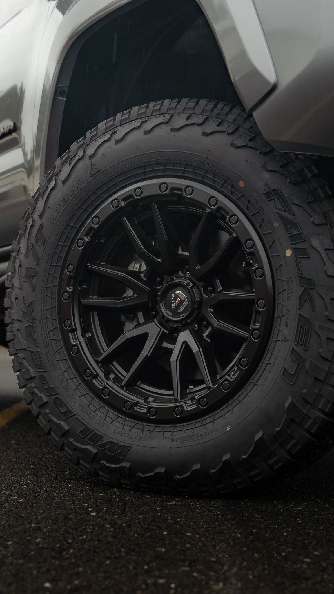 Black truck wheel with off-road tire. Black rim and tire on wet ground.