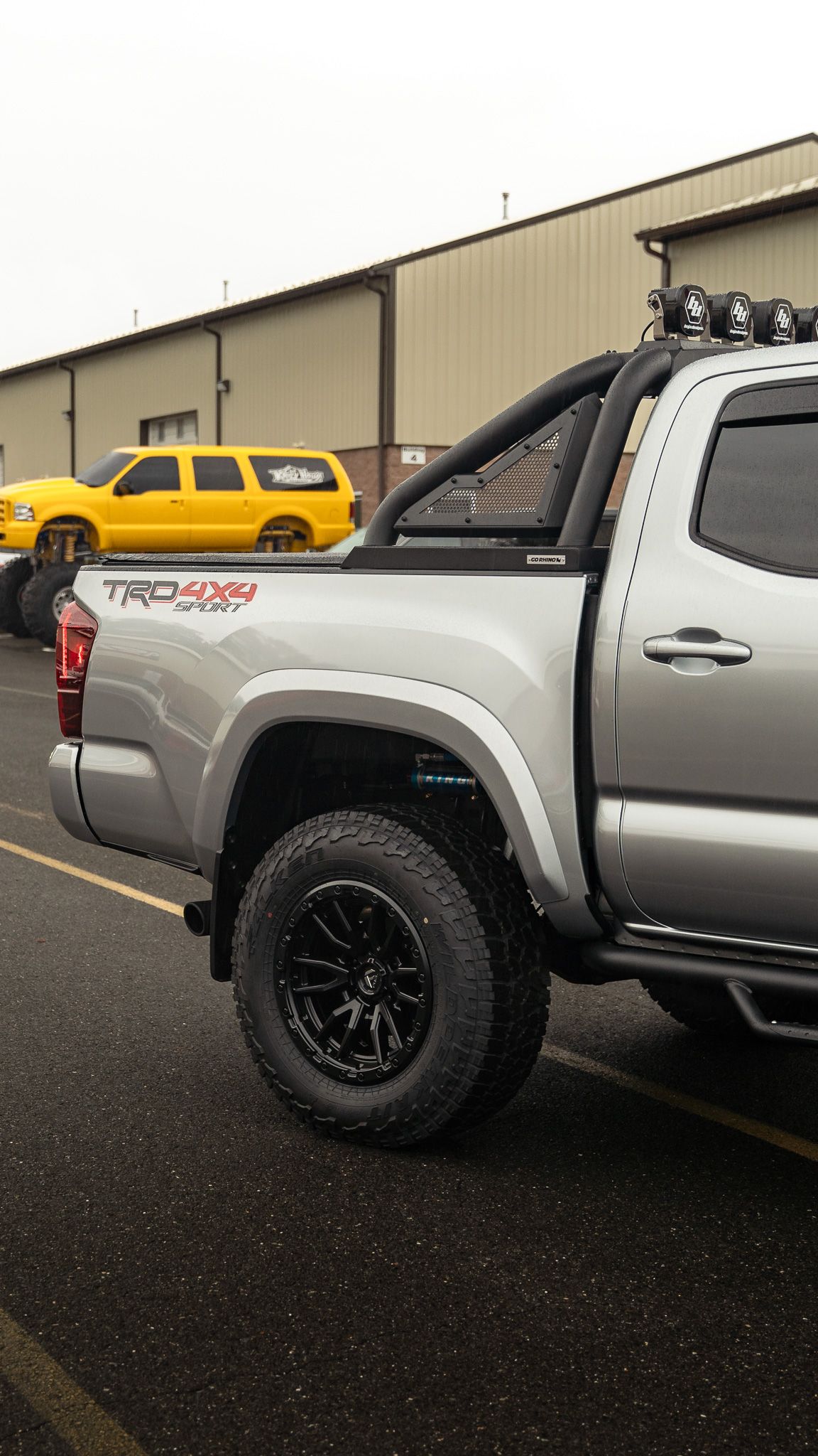 Silver Toyota Tacoma truck with black wheels and a roll bar, parked outdoors.