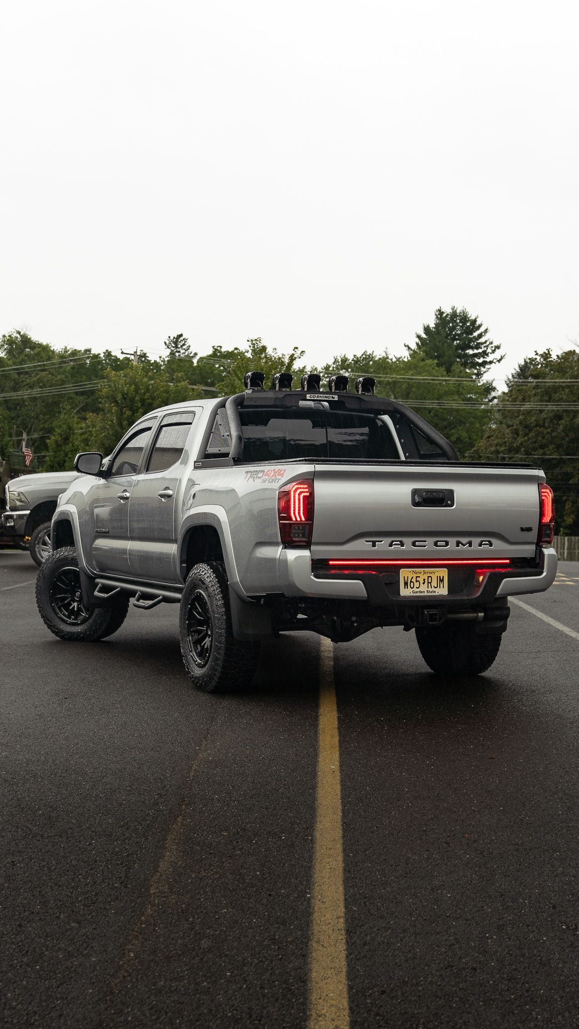Silver Toyota Tacoma truck parked on asphalt, modified with off-road tires and accessories.