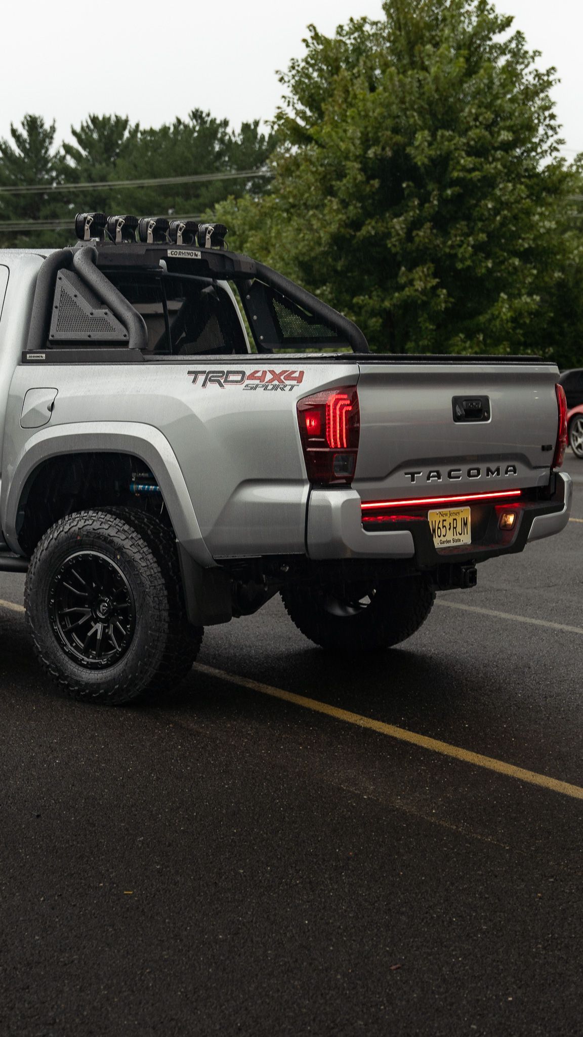 Silver Toyota Tacoma truck, black wheels, off-road accessories, parked on wet asphalt.