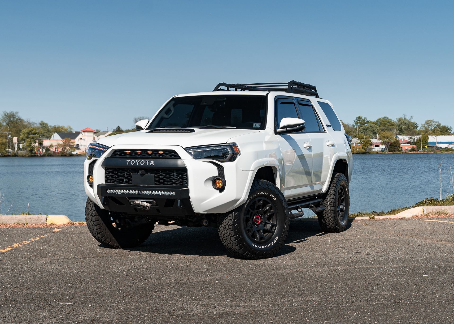 White off-road Toyota 4Runner with black accents parked in front of a body of water on a sunny day.