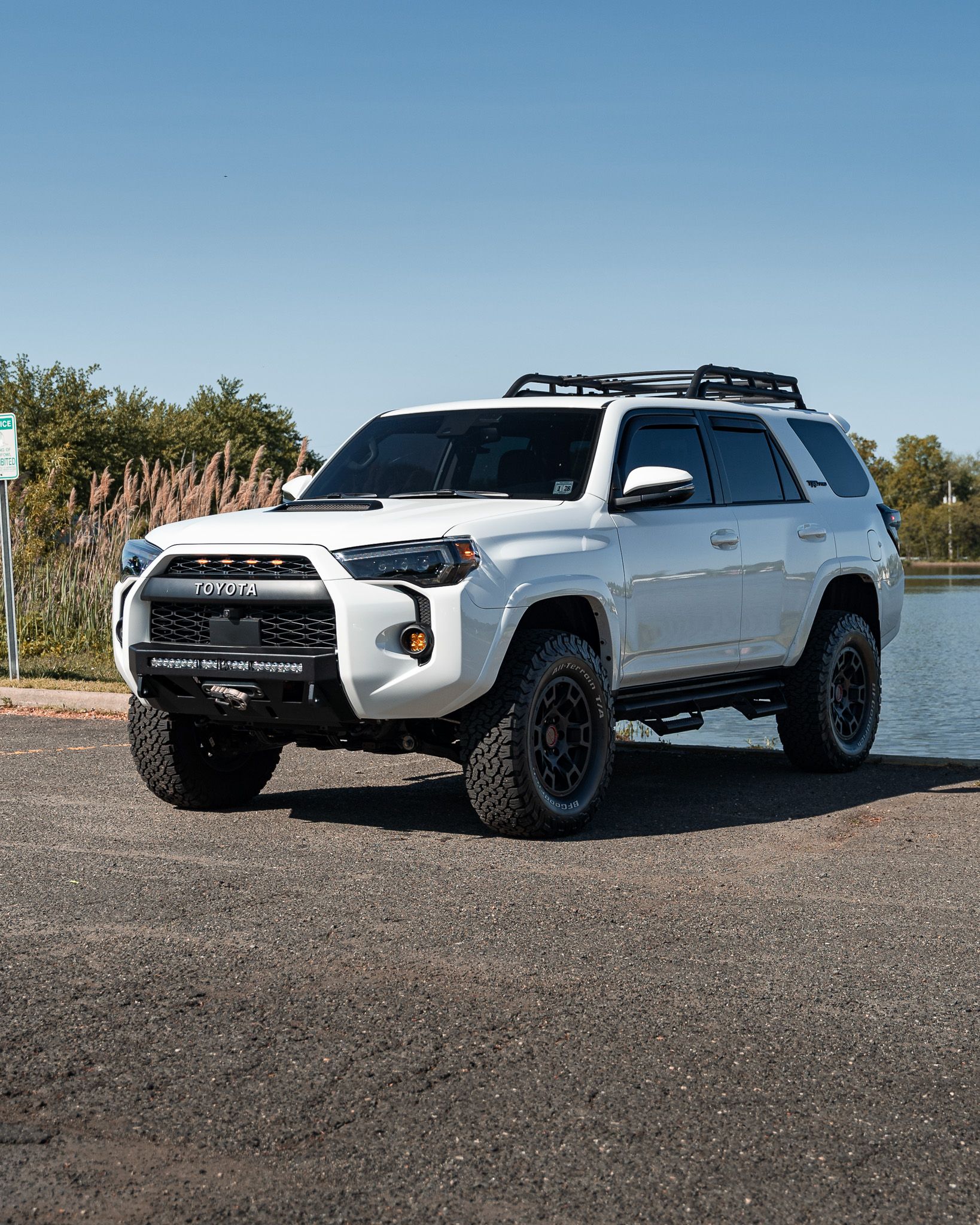 White Toyota 4Runner with black accents parked on gravel near water on a sunny day.
