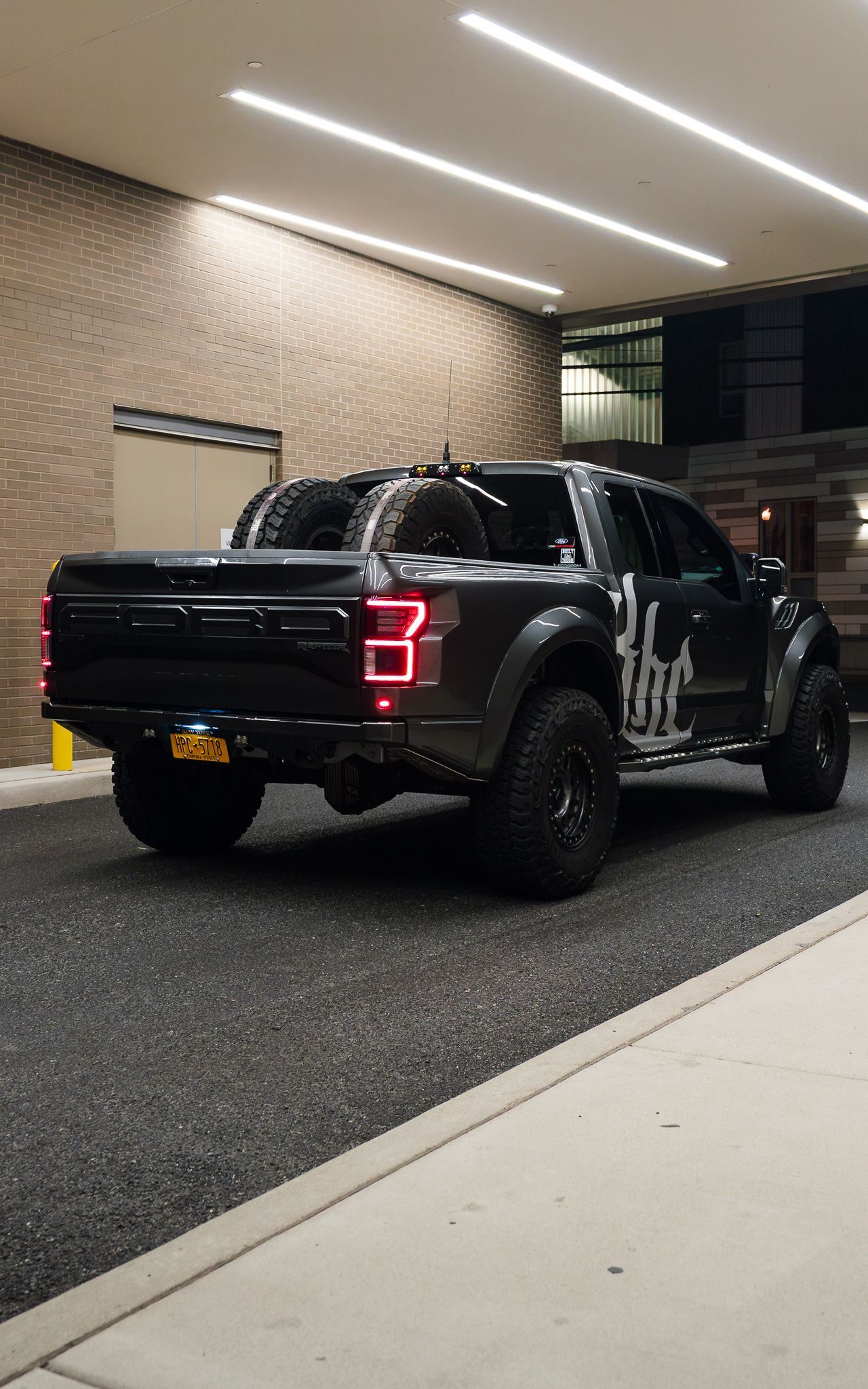 Dark gray Ford Raptor truck parked in front of a building at night.